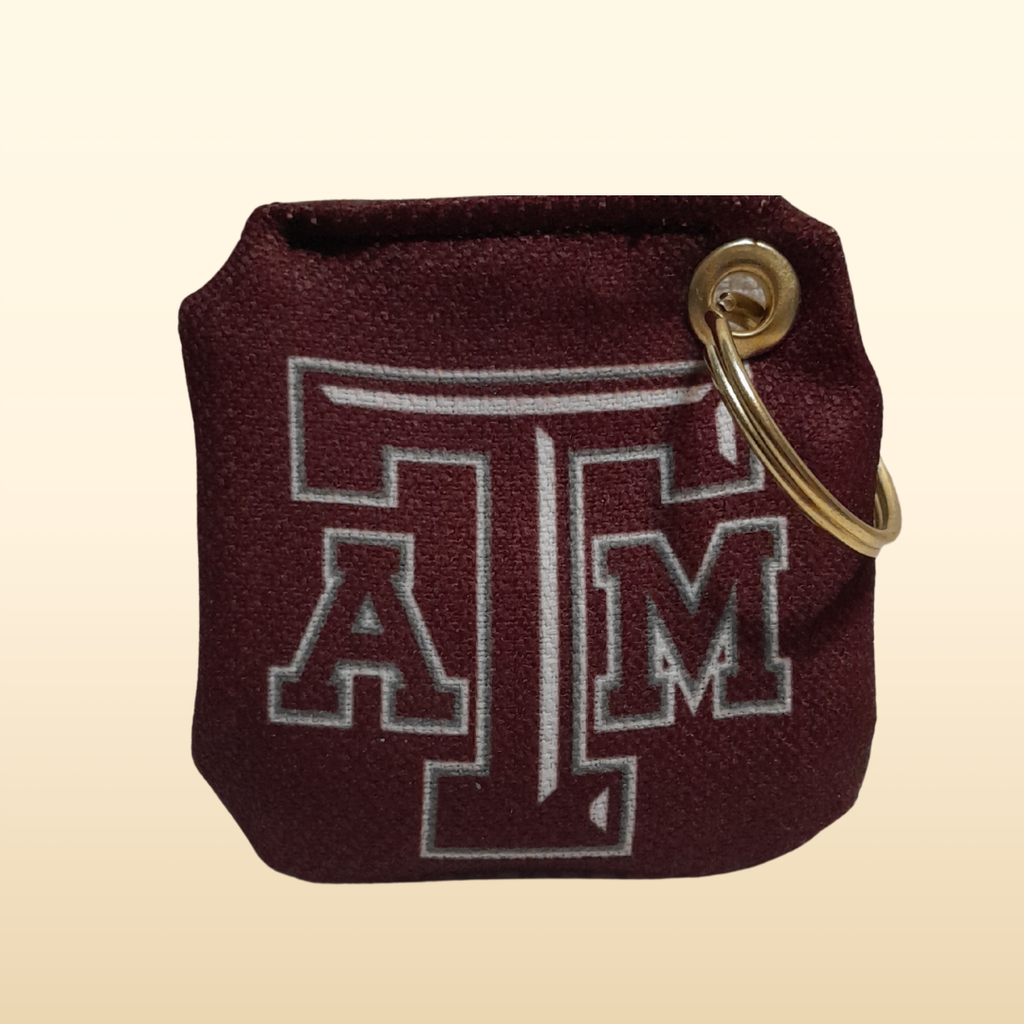 Maroon keychain pouch with gold ring and 'A&M' logo on a beige background