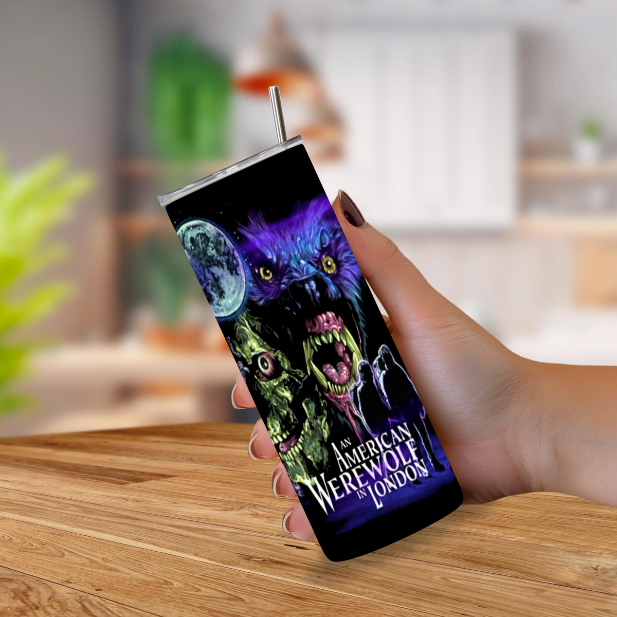 A hand holding a 20oz tumbler with movie graphics from "An American Werewolf in London" on a blurred background 