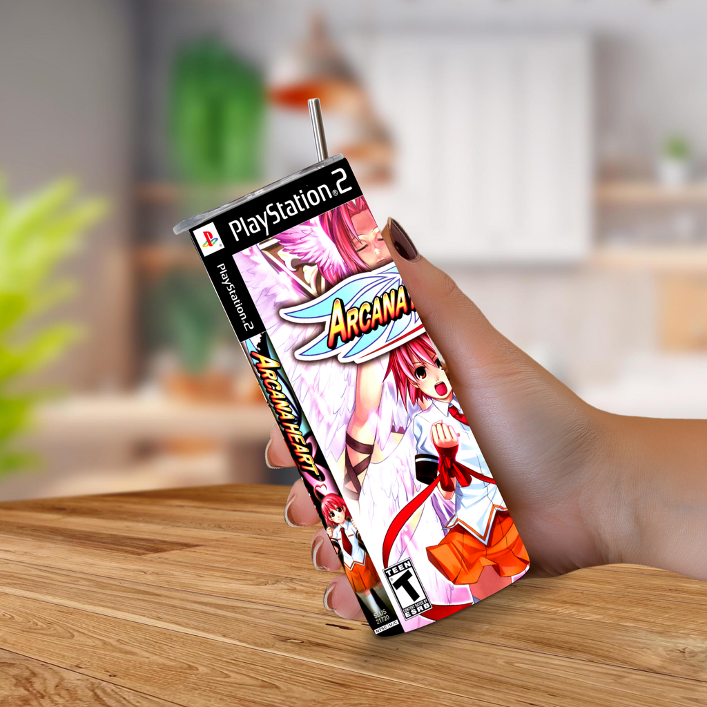 A hand holding a 20oz tumbler PlayStation 2 game designed with Arcana Heart, on a wooden table with a blurred indoor background.