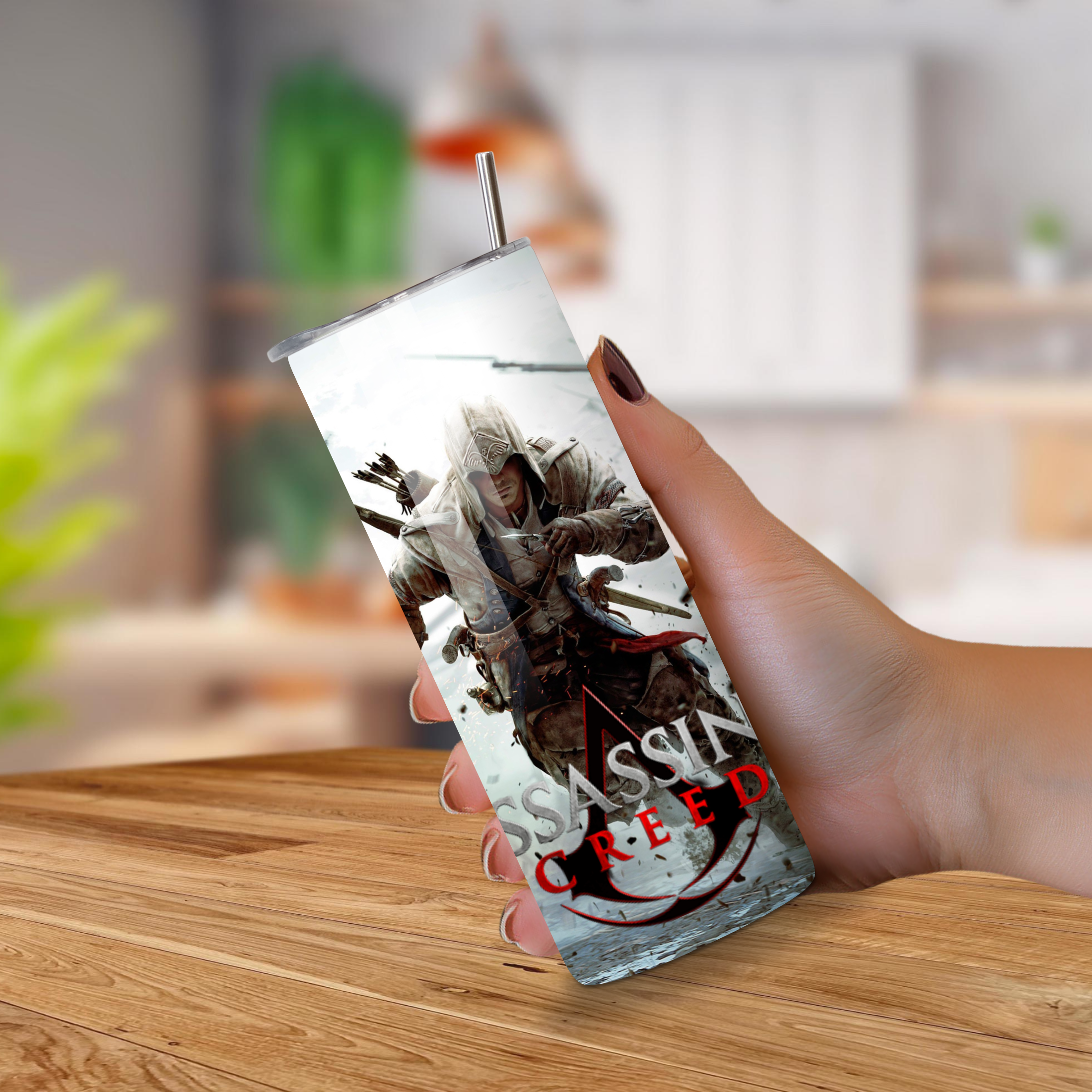 Person holding a 'Assassin's Creed' themed tumbler on a wooden surface.