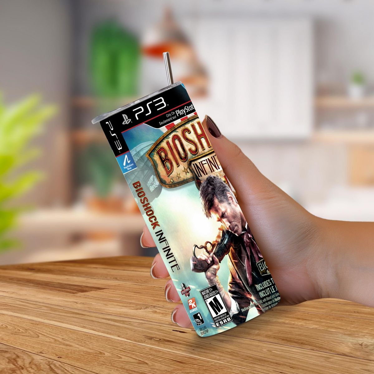 A hand holding a 20oz stainless steel ps3 'BioShock Infinite' theme tumbler, on a blurred kitchen background.