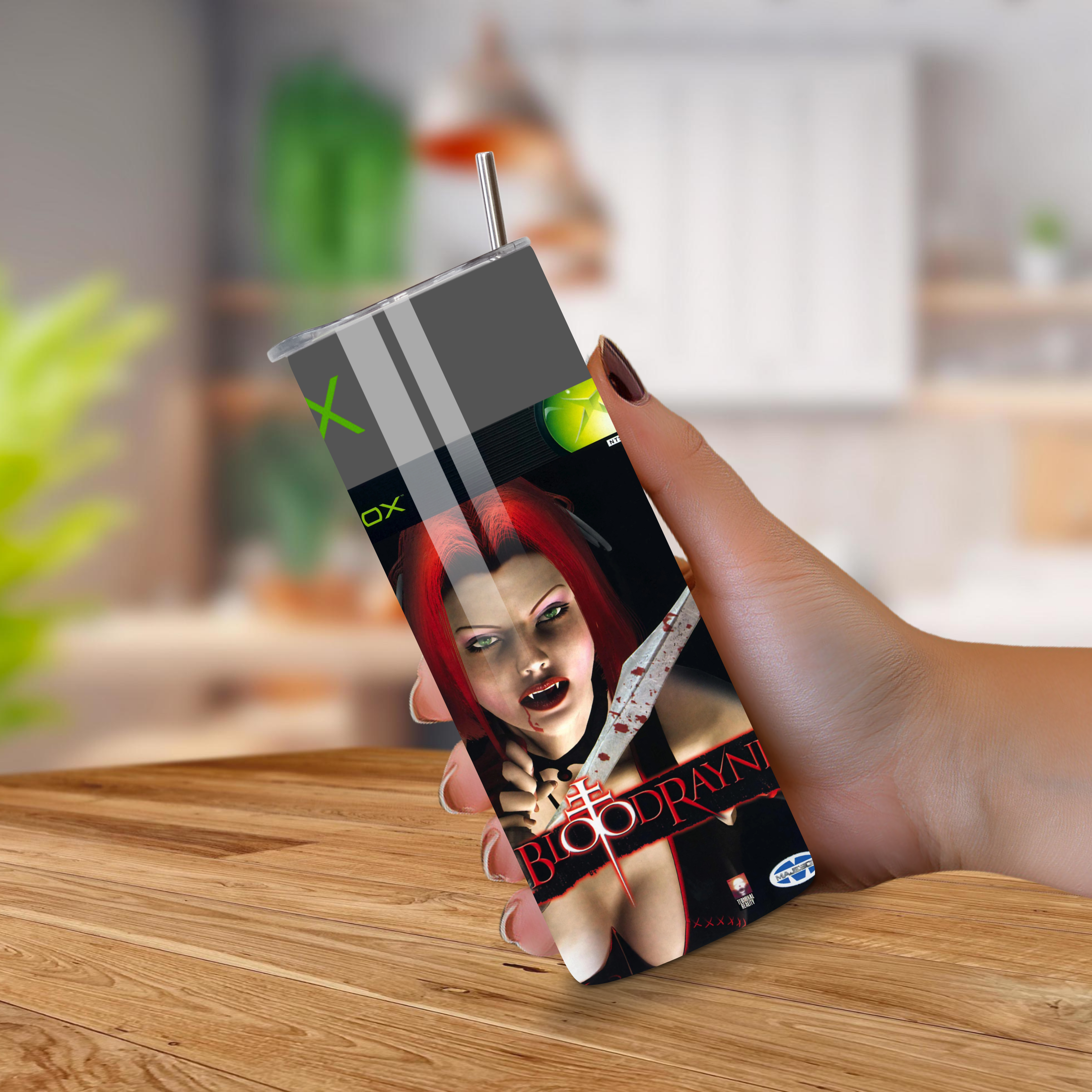 Tumbler with a graphic design of a woman holding a knife, labeled 'Bloodrayne', held by a hand on a wooden surface.