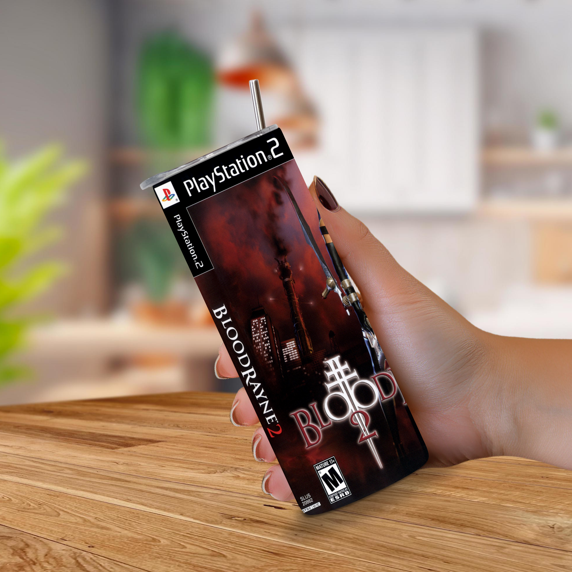 A hand holding a PlayStation 2-themed 20oz stainless steel tumbler with a straw, featuring the Bloodrayne 2 video game cover art, set against a blurred indoor background.