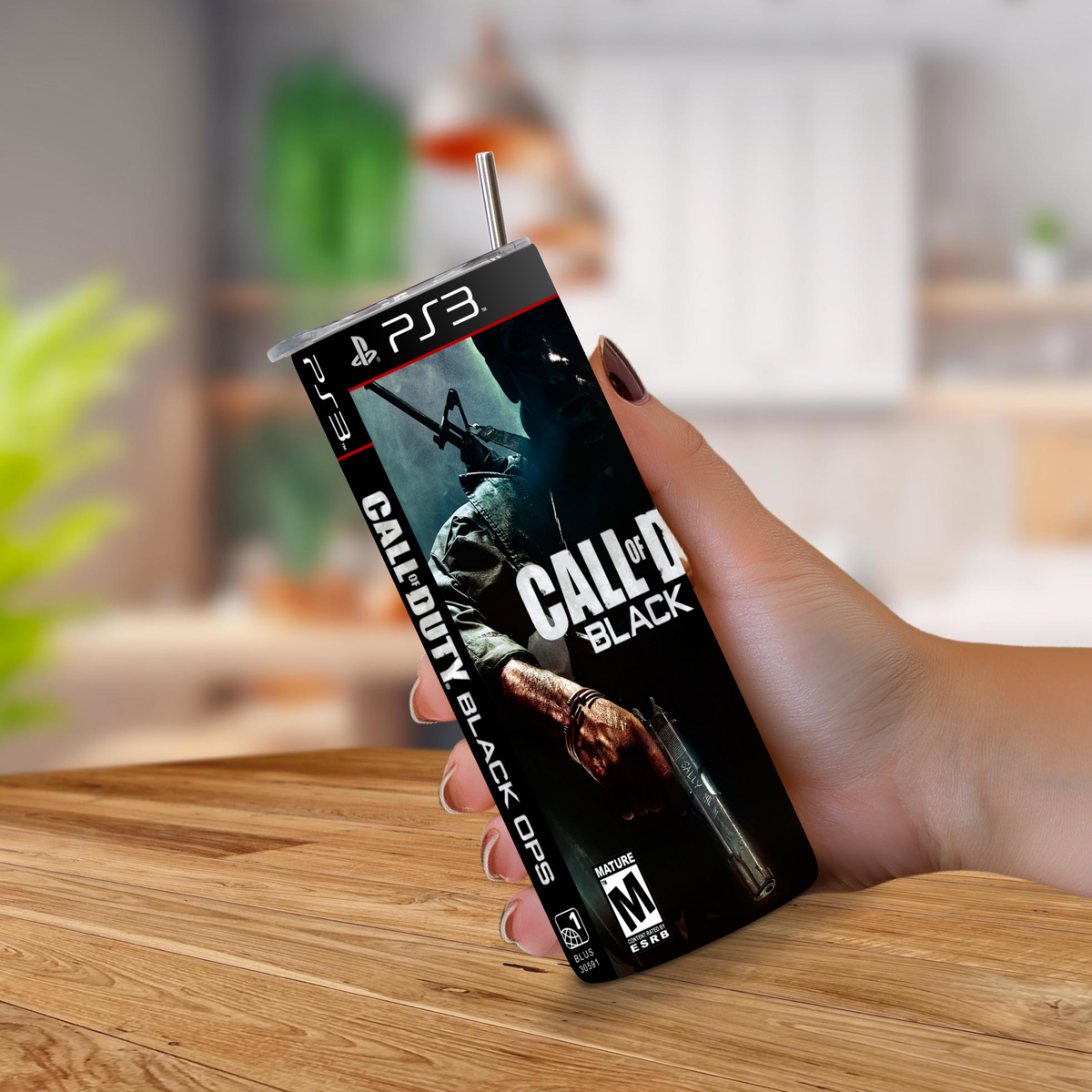 A hand holding a PS3-shaped 20oz stainless steel tumbler can featuring the Call of Duty: Black Ops game cover art, set against a blurred indoor background.