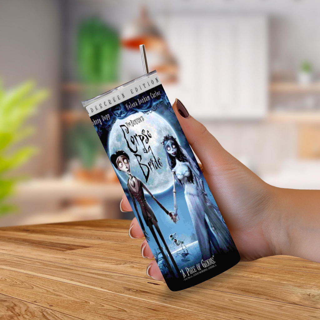 A hand holding a 20oz insulated tumbler with a straw, printed with Corpse Bride under a full moon, set against a blurred kitchen background.