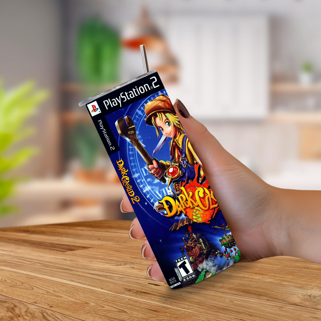 A hand holding a 20oz stainless steel tumbler shaped like a PlayStation 2 Dark Cloud 2 game cover, with a metal straw sticking out of the top, set against a blurred indoor background.