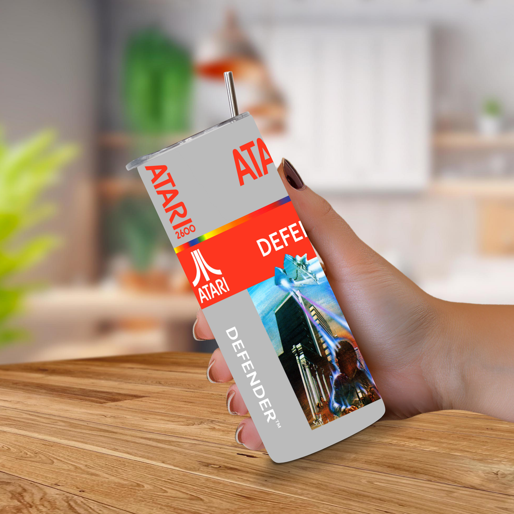 A hand holding a custom-printed Atari 2600 defender themed tumbler cup with a straw, set against a blurred kitchen background.