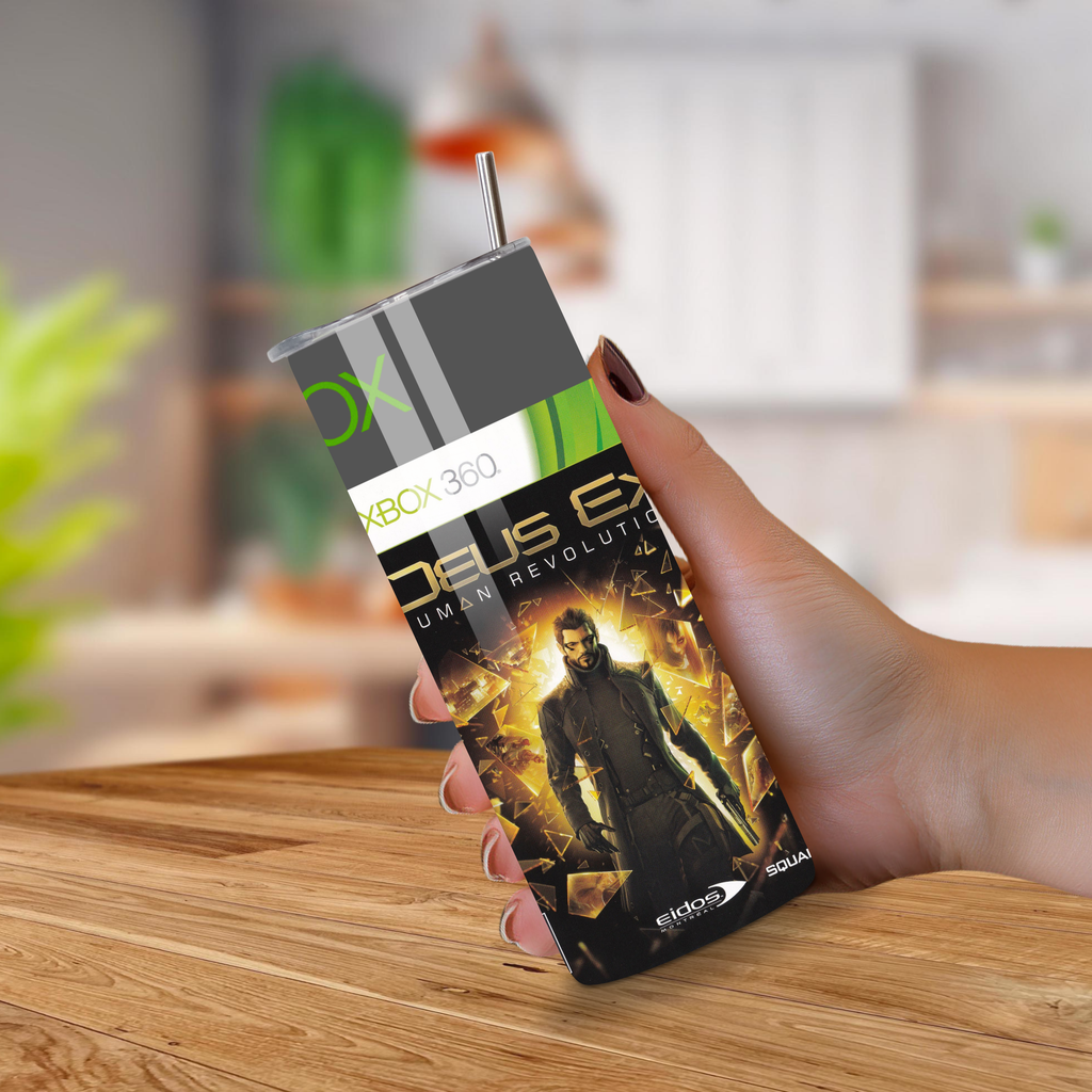 Hand holding a ' Deus Ex: Human Revolution ' Xbox 360 game tumbler on a wooden surface.