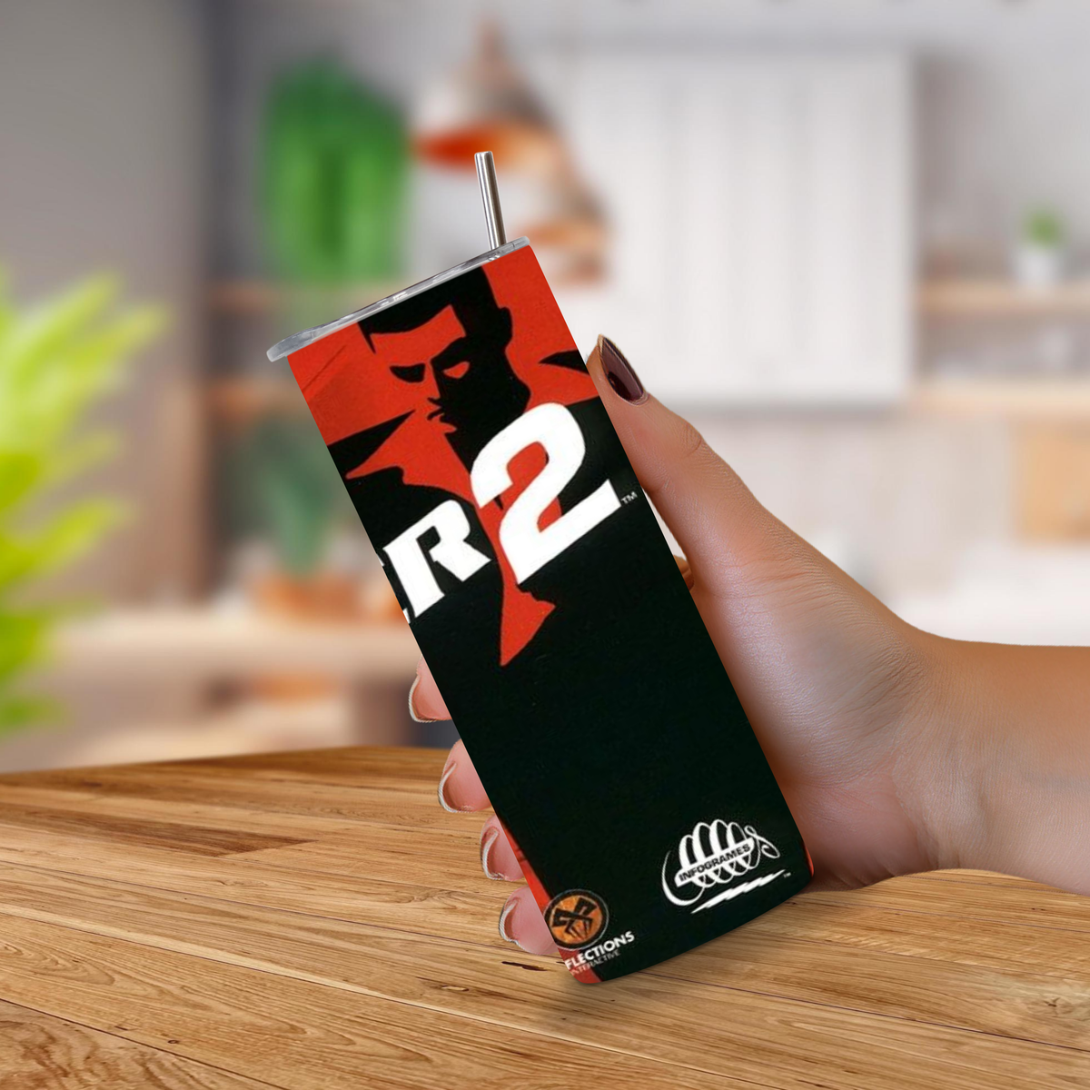 A hand holding a Driver 2 design 20oz stainless tumbler with a metal straw, set against a blurred kitchen background.