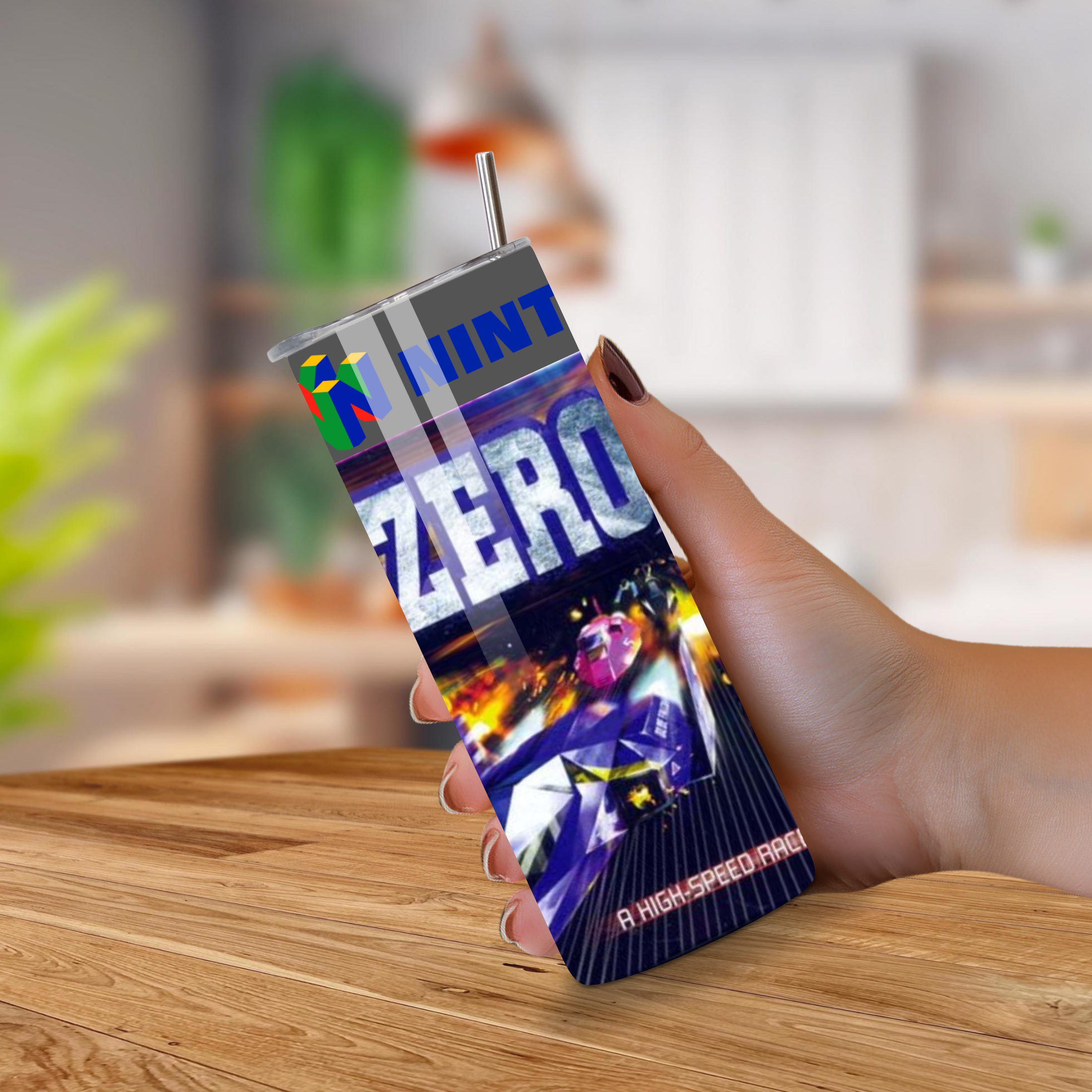 Person holding a tumbler with F-Zero X design with a straw on a wooden surface.