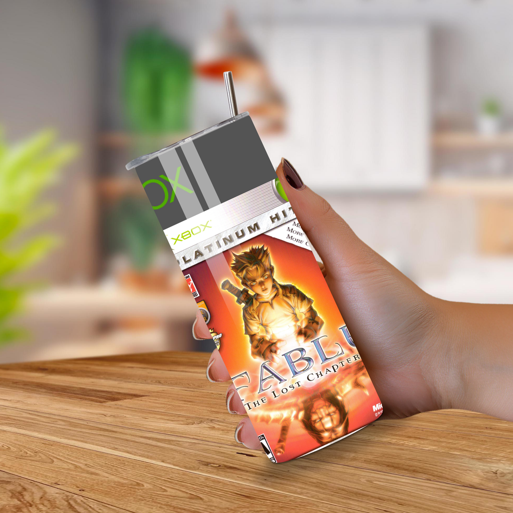 Hand holding a tumbler with a 'Fable' game graphics on a wooden surface