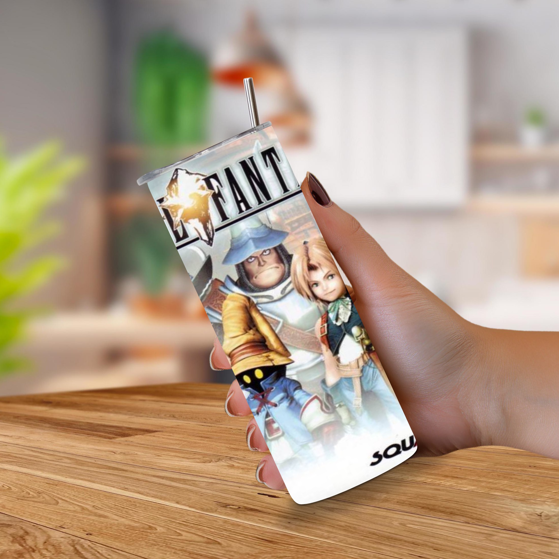 A hand holding a 20oz stainless steel tumbler with a metal straw, featuring a printed 'Final Fantasy IX' video game character design, set against a blurred indoor background.