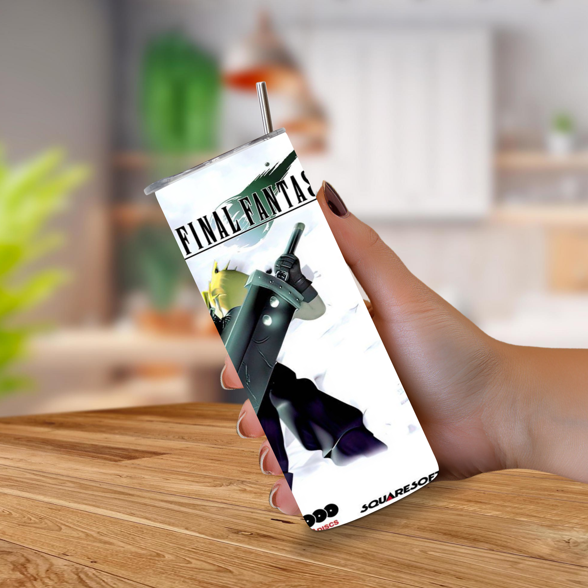 A hand holding a 20oz tumbler with a straw, featuring Final Fantasy VII artwork on the cup, set against a blurred indoor background with a wooden table.