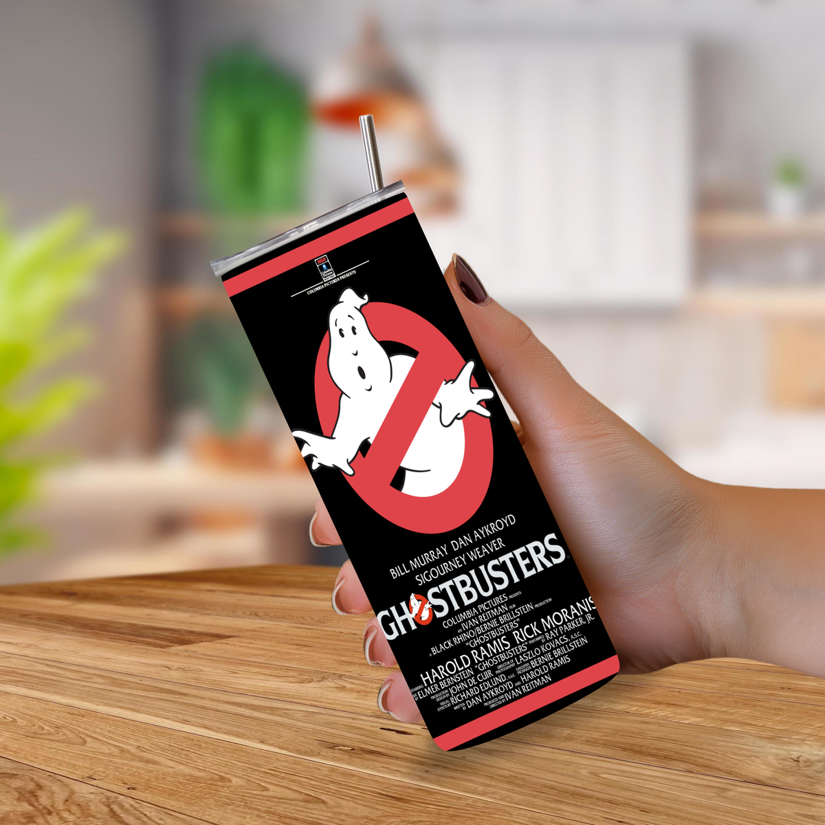 A hand holding a 20oz tumbler with "Ghostbusters" movie graphics design on a blurred background. 