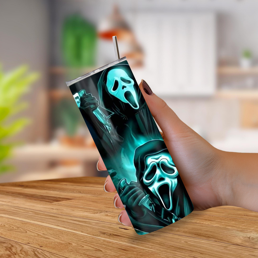 A hand holding a tall insulated tumbler with a metal straw, featuring a printed graphic of two Ghostface figures in glowing teal masks against a dark background, set against a blurred indoor kitchen backdrop.