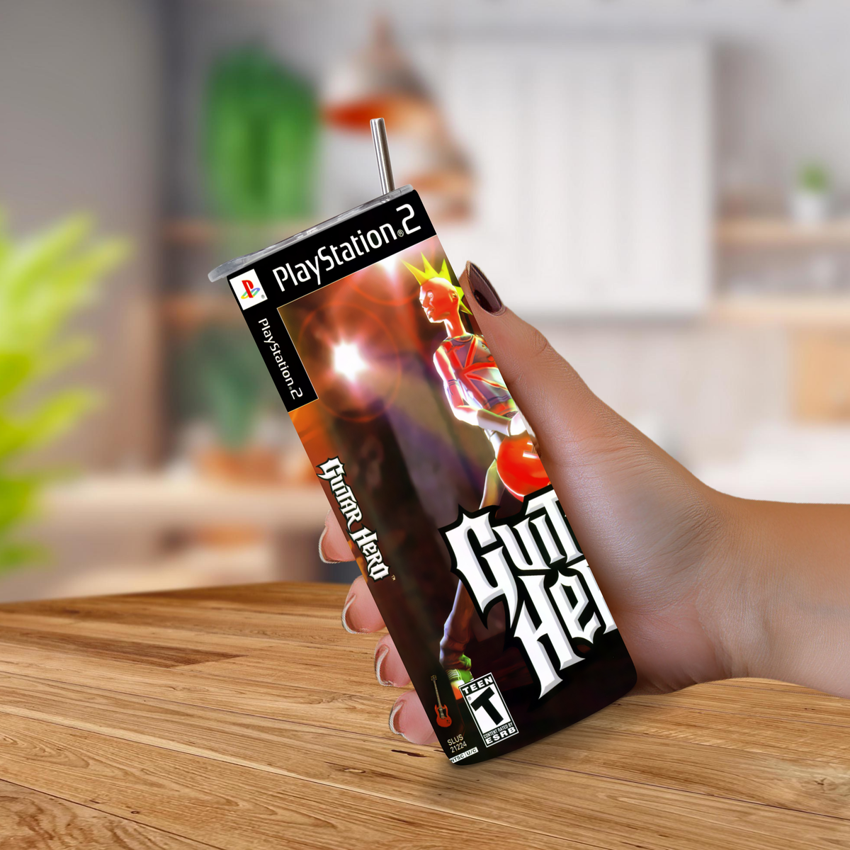 A hand holding a 20oz tumbler PlayStation 2 themed drink cup designed to look like a Guitar Hero, set against a blurred kitchen background.