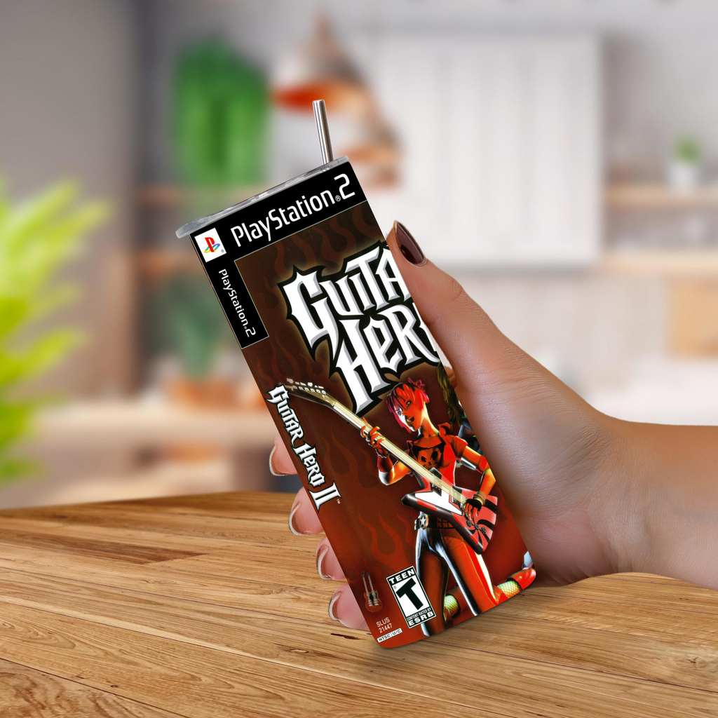 A hand holding a PlayStation 2 themed 20oz tumbler with a straw, featuring the Guitar Hero II cover art, set against a blurred indoor background.