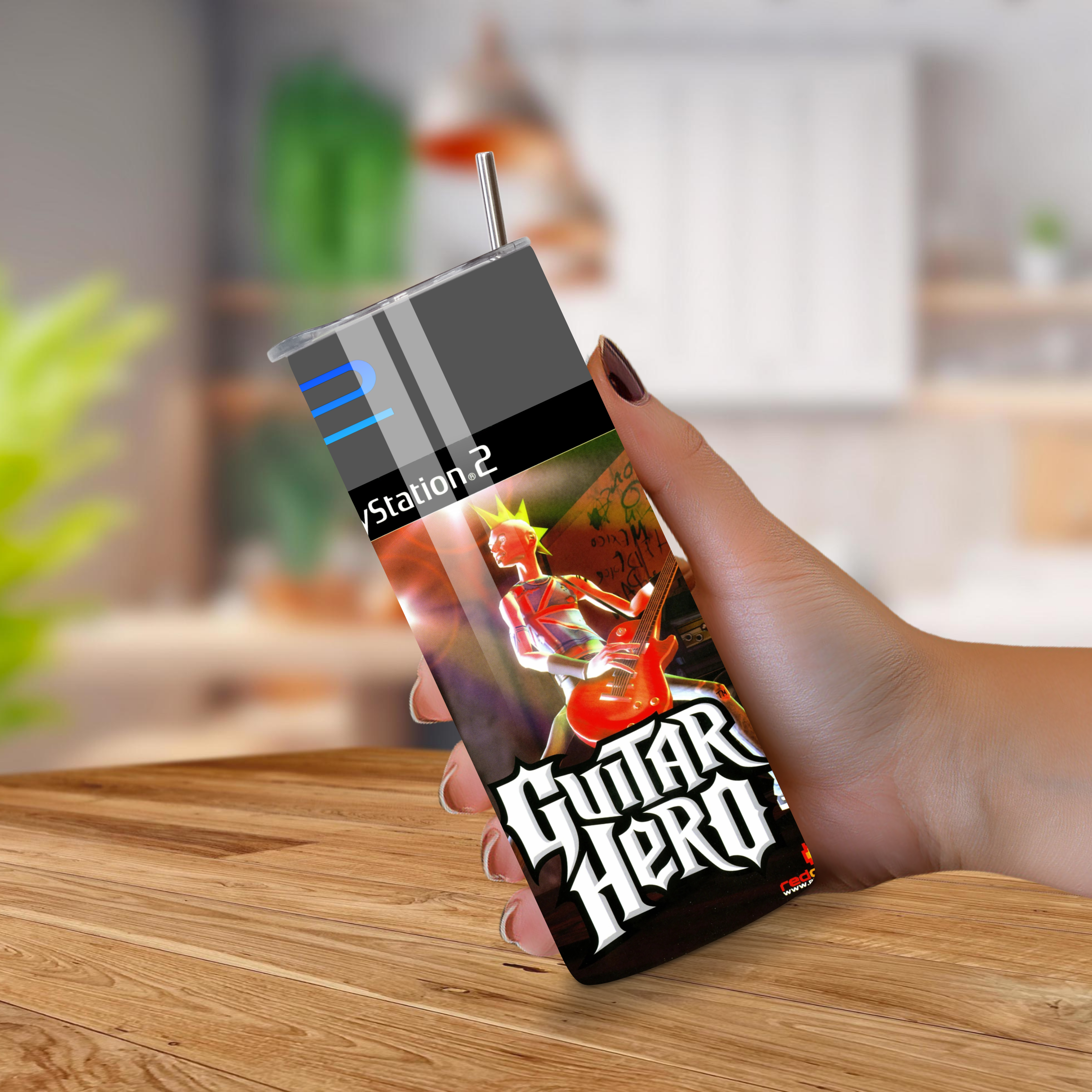 Hand holding a Guitar Hero PlayStation 2 tumbler on a wooden surface with a blurred background