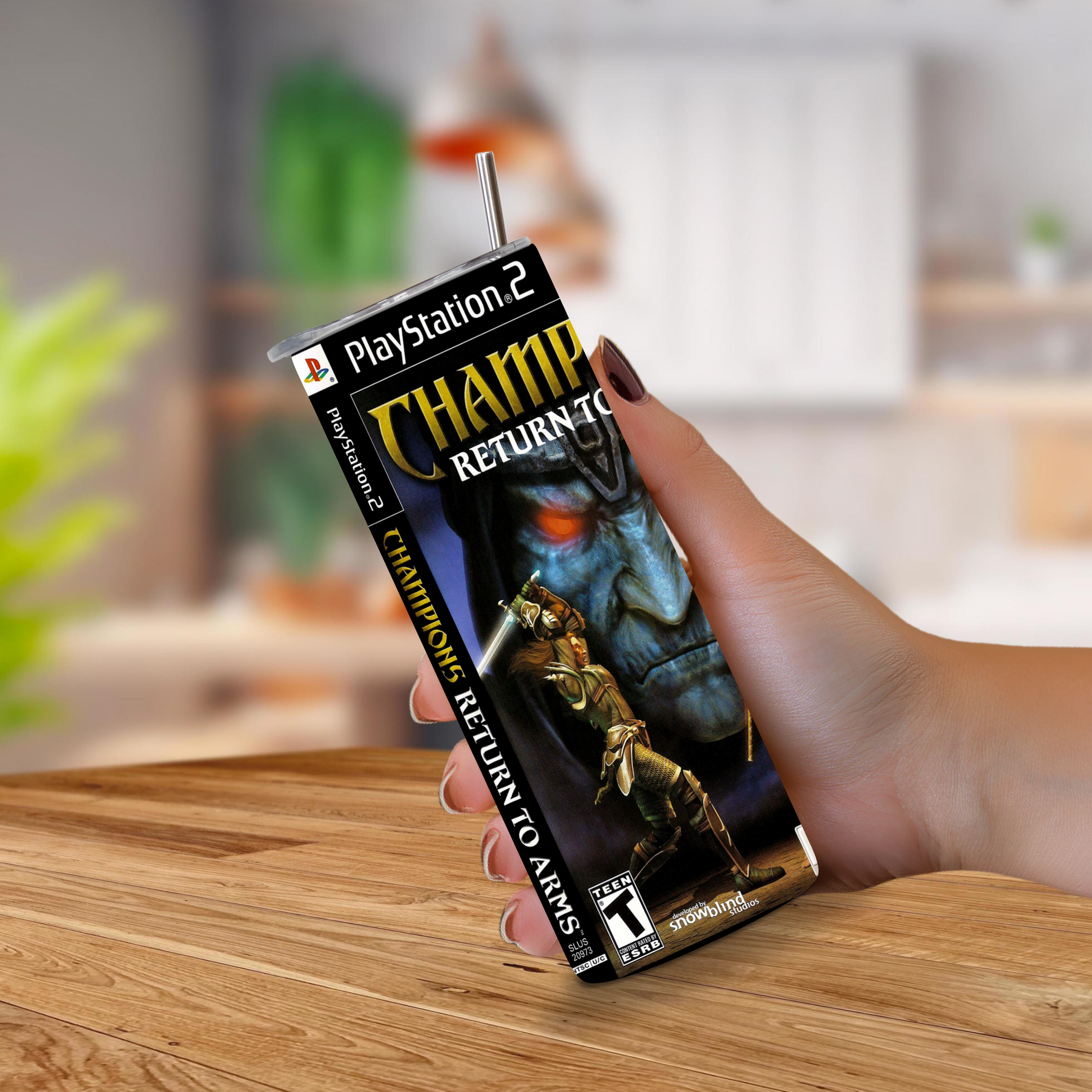 A hand holding a PlayStation 2 game cover designed to look like a 20oz stainless steel tumbler, featuring the game Champions Returns to Arms, with a metal straw sticking out of the top, set against a blurred indoor background.