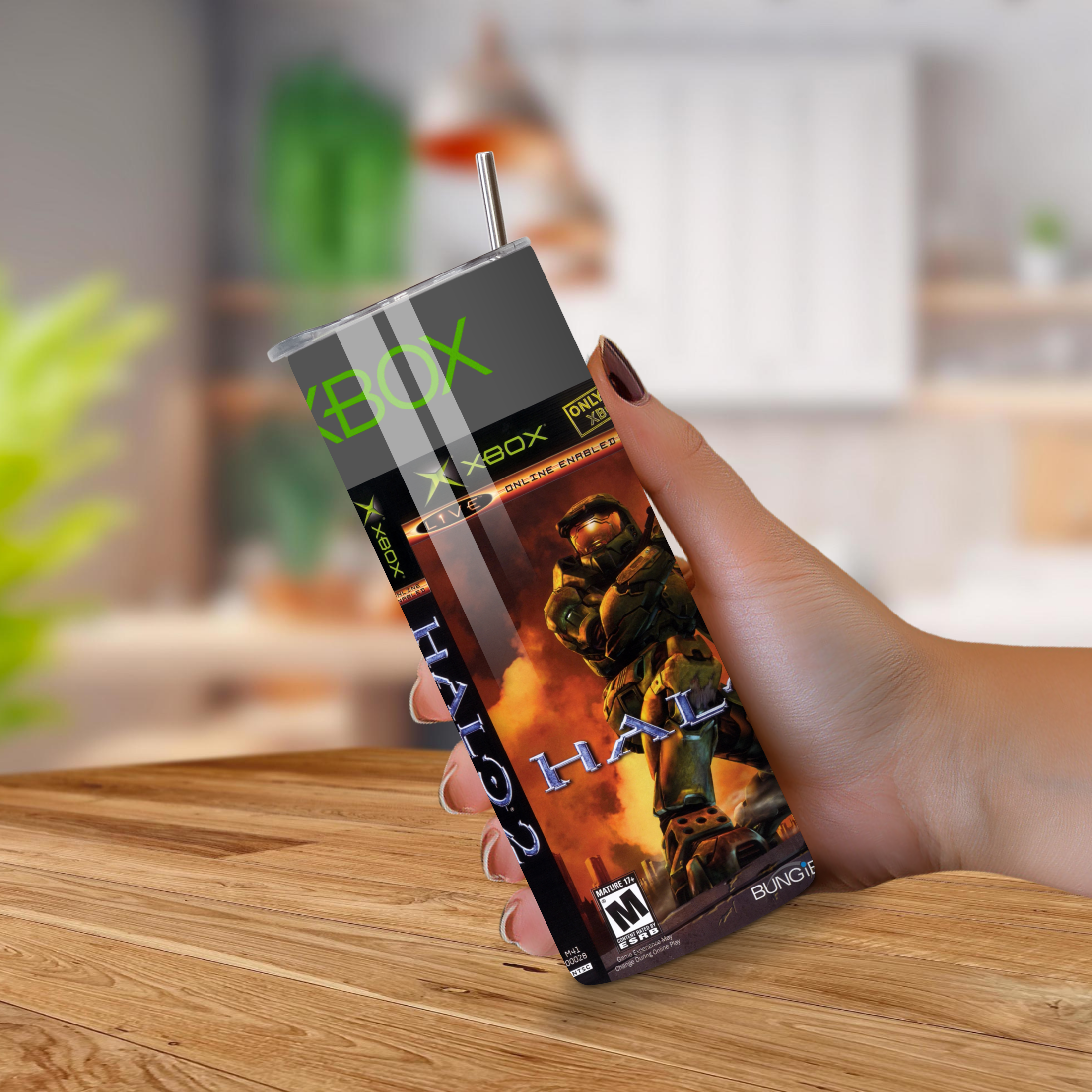Hand holding a Halo-themed Xbox tumbler on a wooden surface with a blurred indoor background
