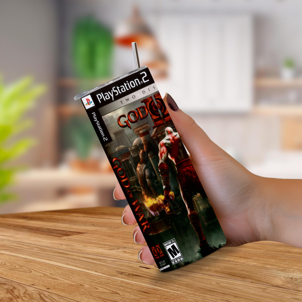 A hand holding a 20oz stainless steel tumbler designed to look like a PlayStation 2 God of War II game cover, set against a blurred kitchen background.