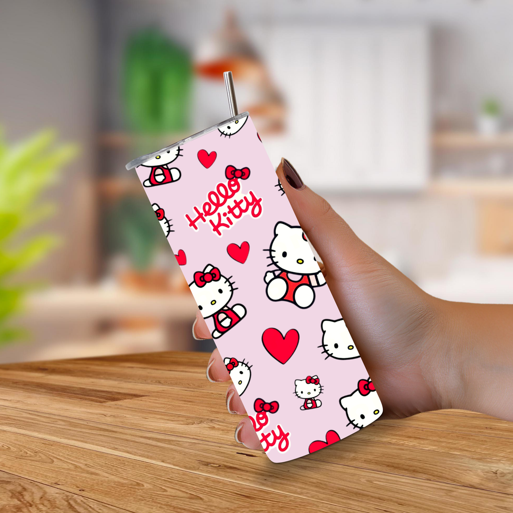 A hand holding a pink Hello Kitty patterned tumbler with a metal straw, set against a blurred indoor background with a wooden table.
