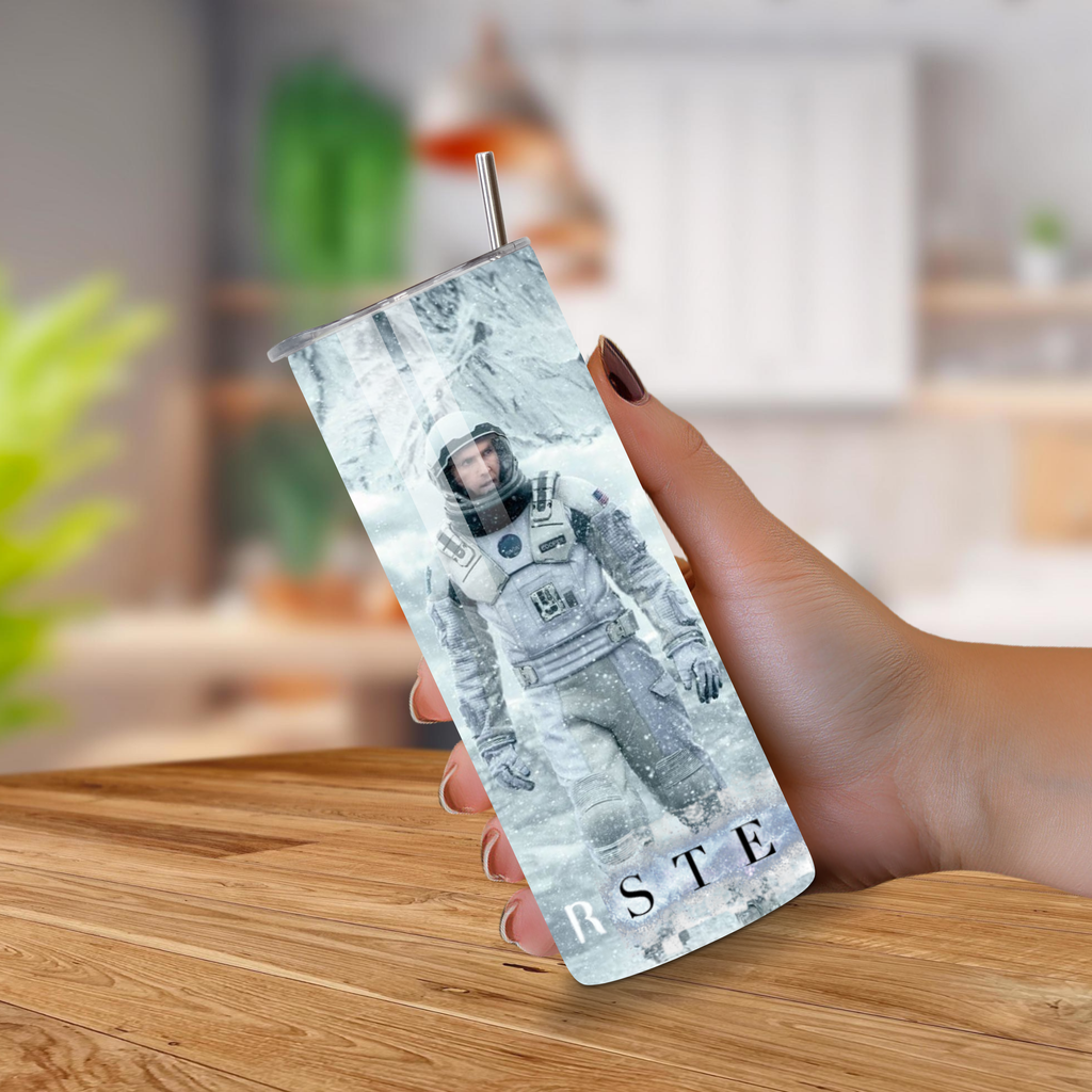 Person holding a tumbler with an Interstellar astronaut design on a wooden surface 