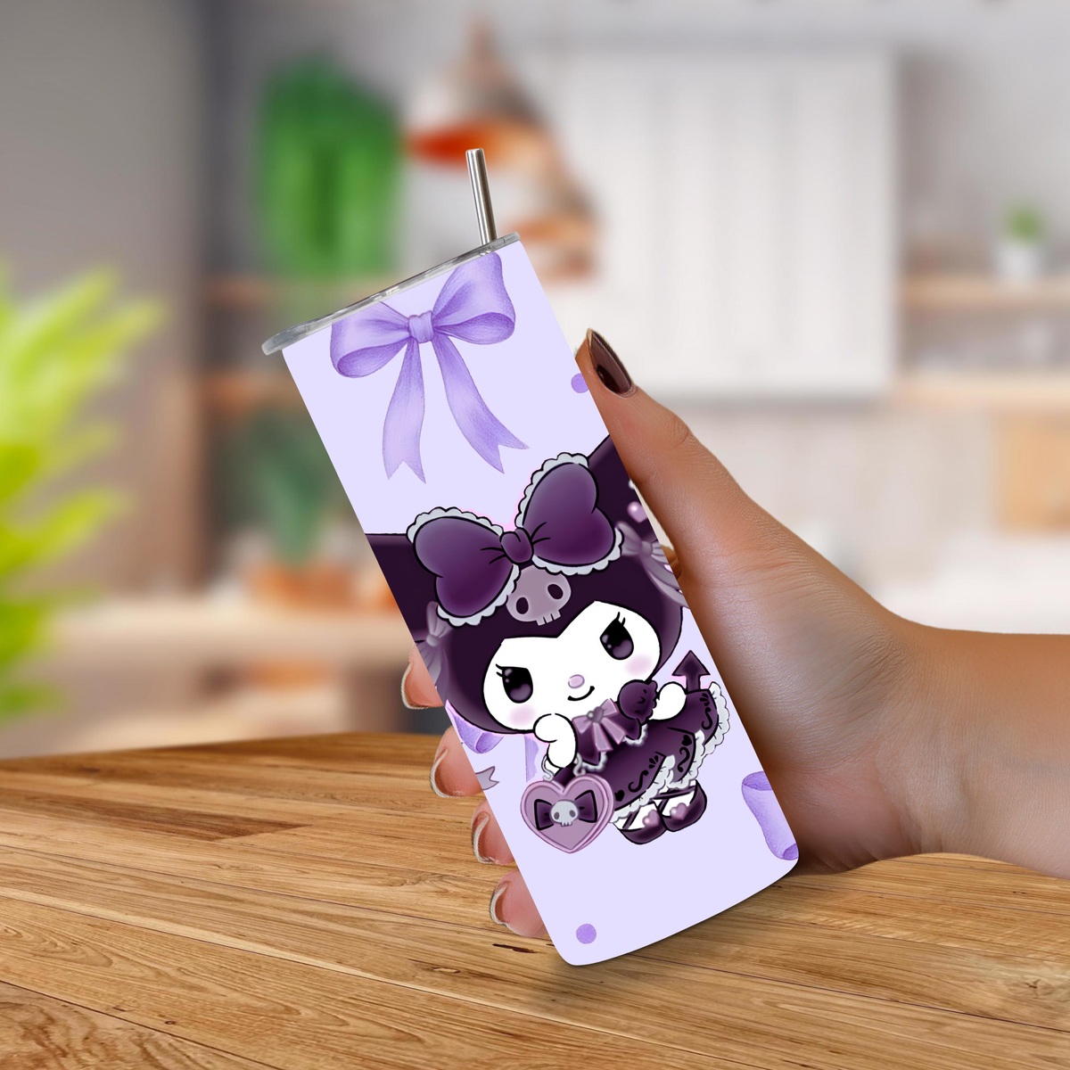 A hand holding a 20oz tumbler with a straw, featuring a purple Kuromi character print and a large purple bow graphic near the top, set against a blurred indoor background.