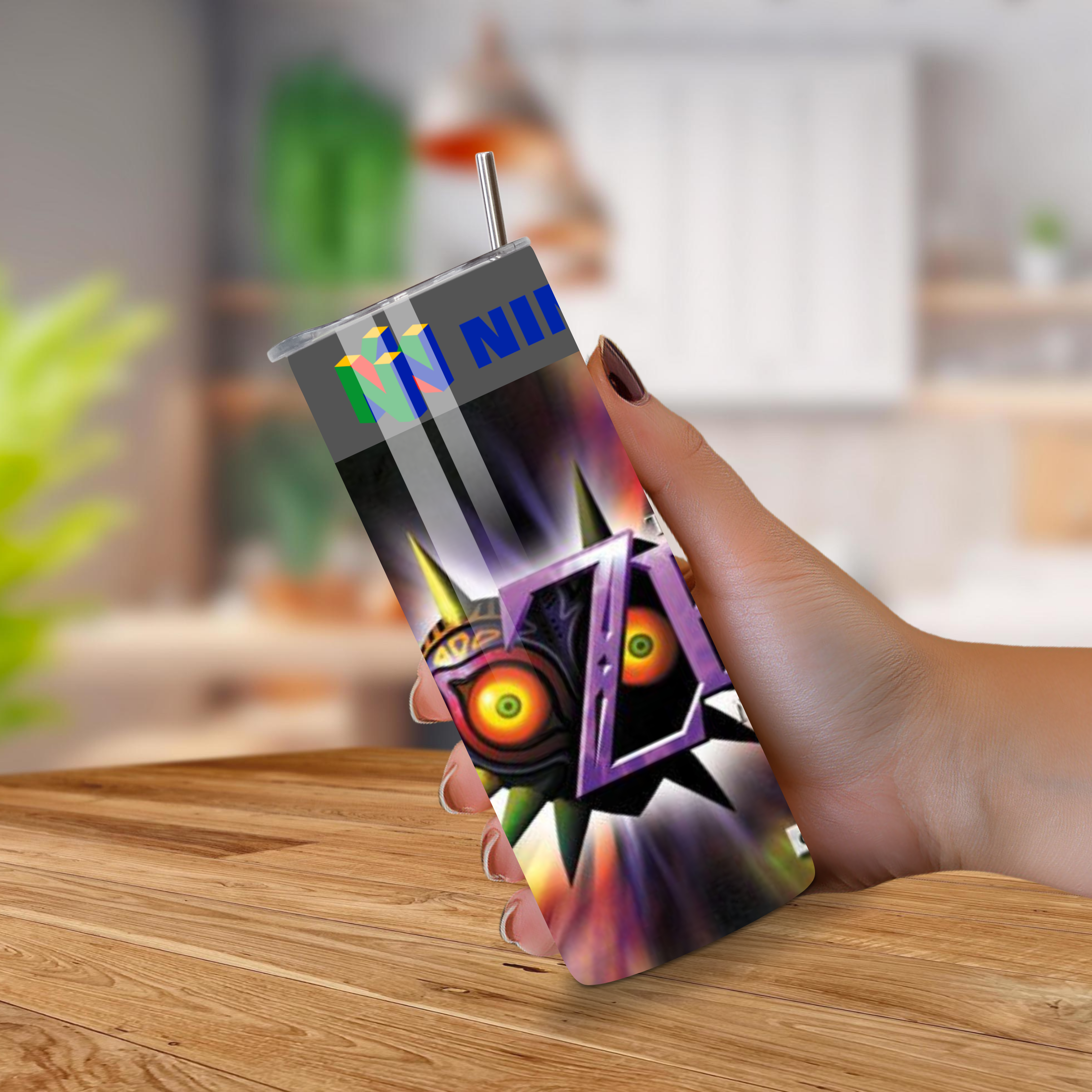 Person holding a majora's mask tumbler with a design on a wooden surface