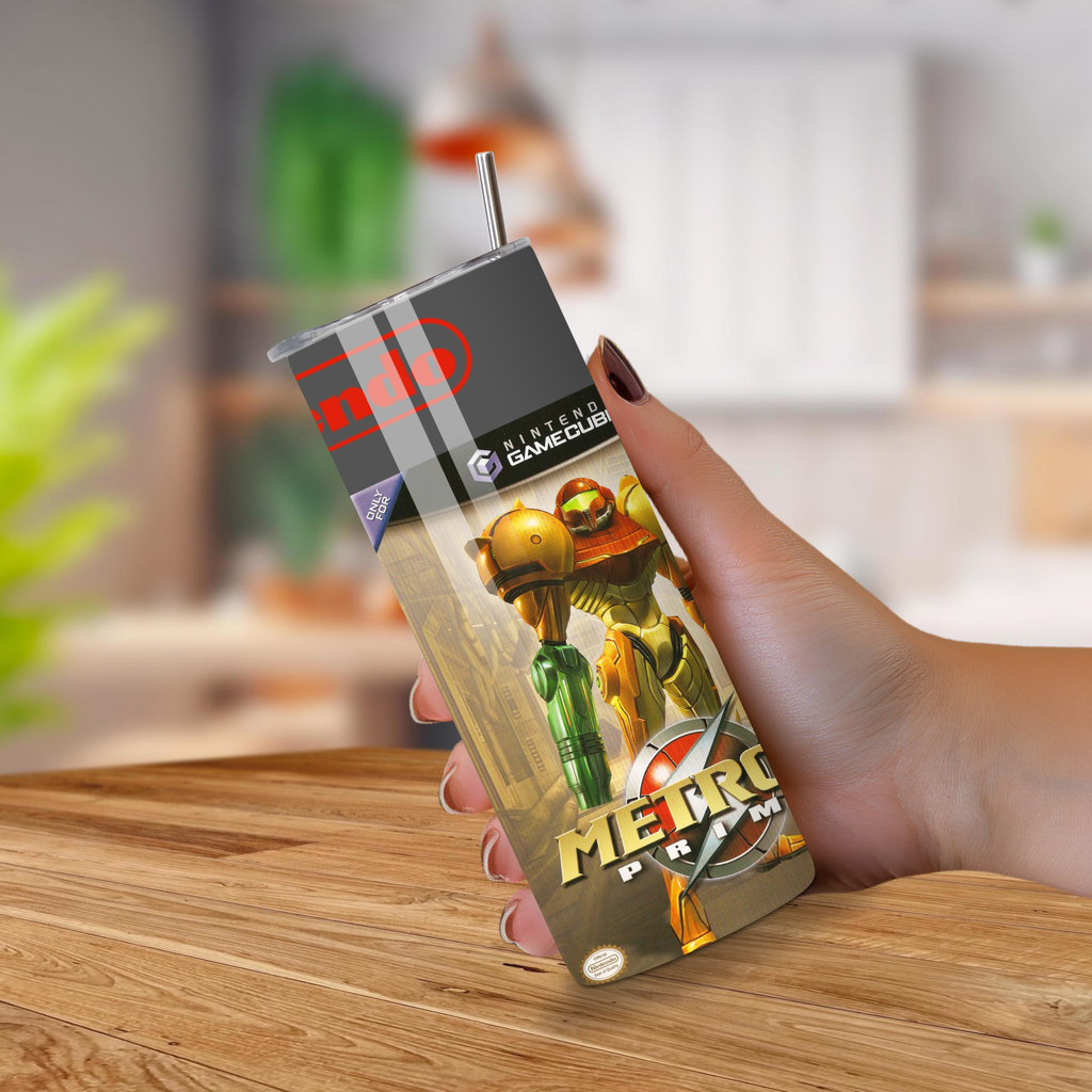 Hand holding a 20oz tumbler with Metroid Prime design on a wooden surface.
