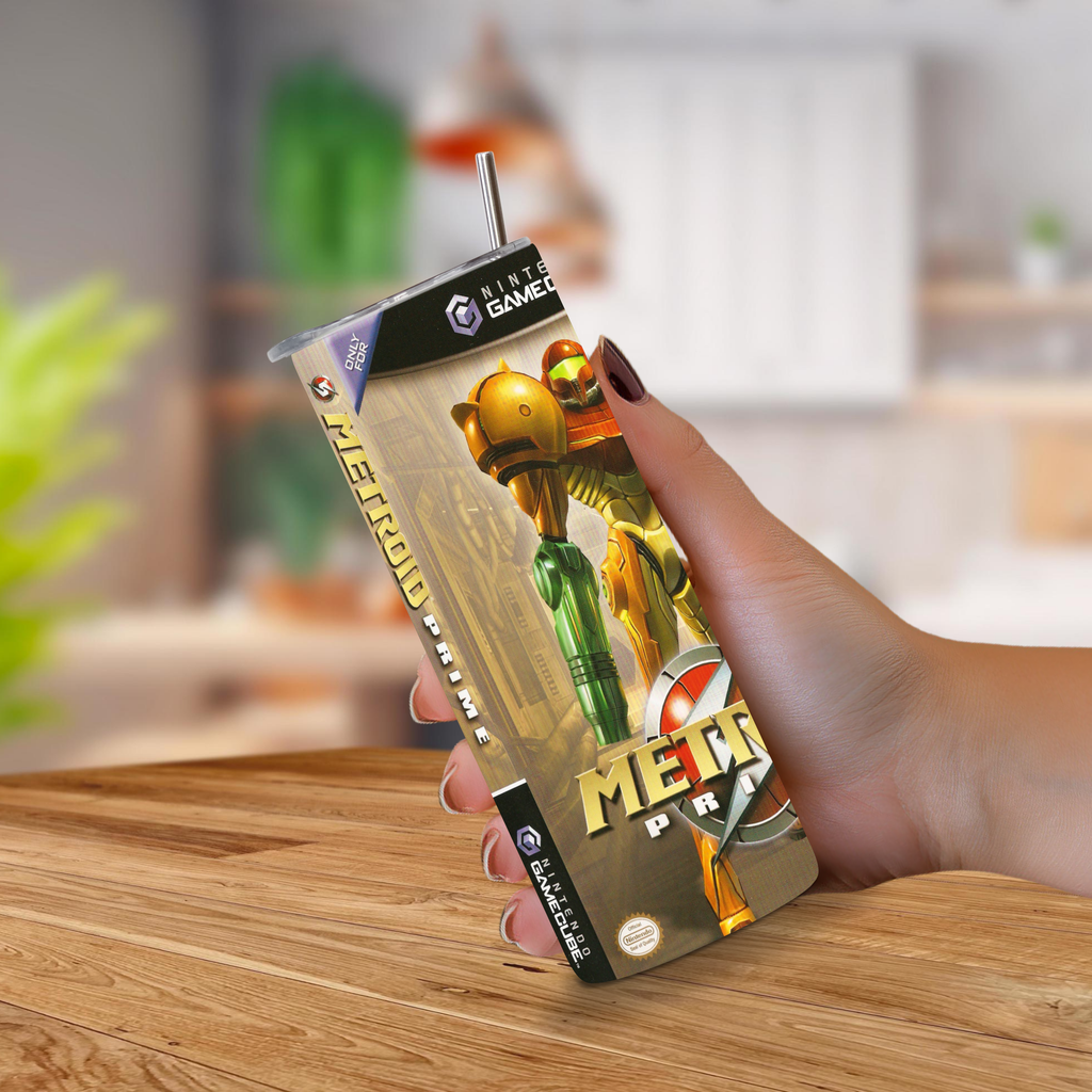 Hand holding a 20oz stainless steel Metroid Prime tumbler featuring A GameCube Theme. On a Blurred kitchen background.