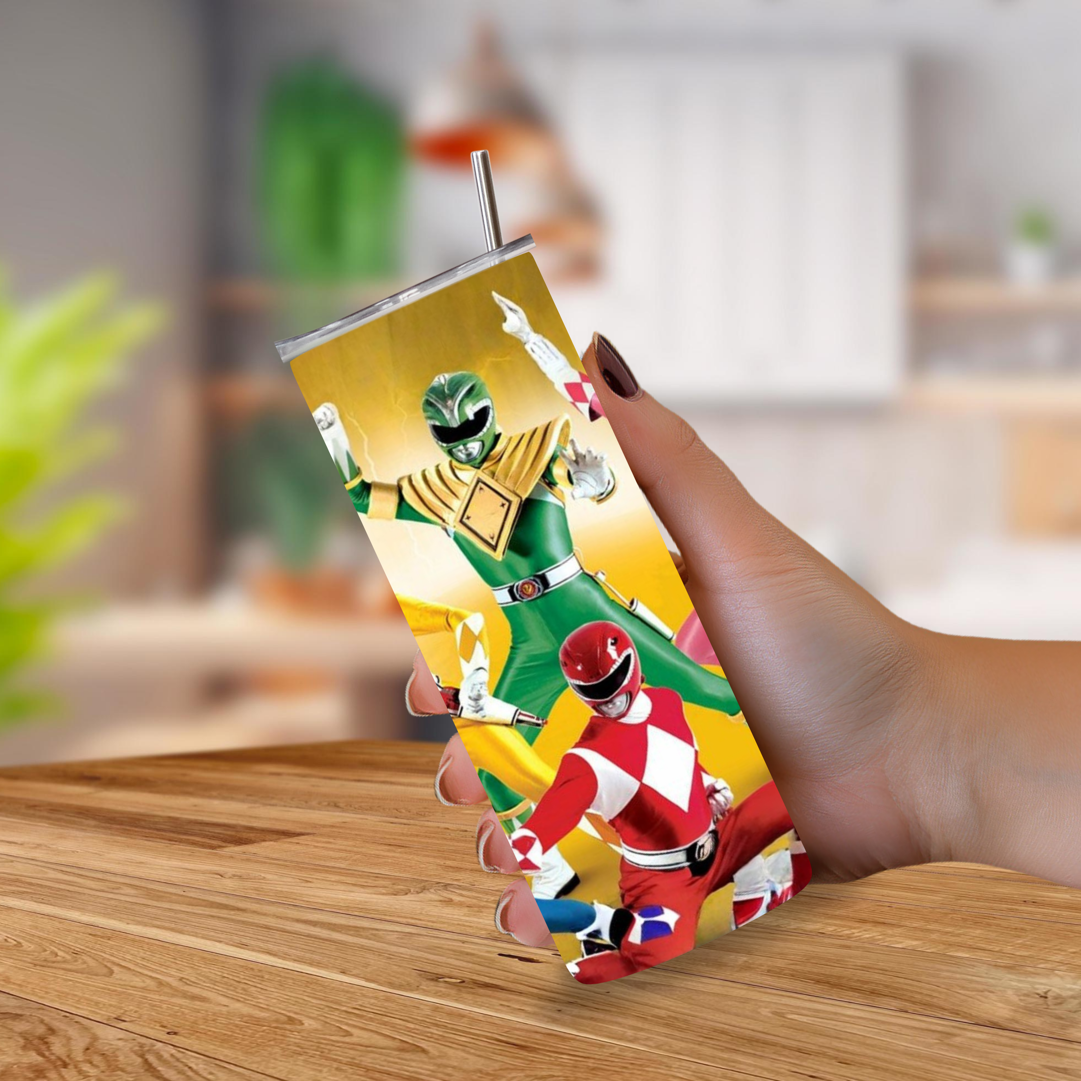 A hand holding a 20oz tumbler with a printed Power Rangers design, featuring the Green Ranger, Red Ranger, and Yellow Ranger on a yellow background, with a metal straw.