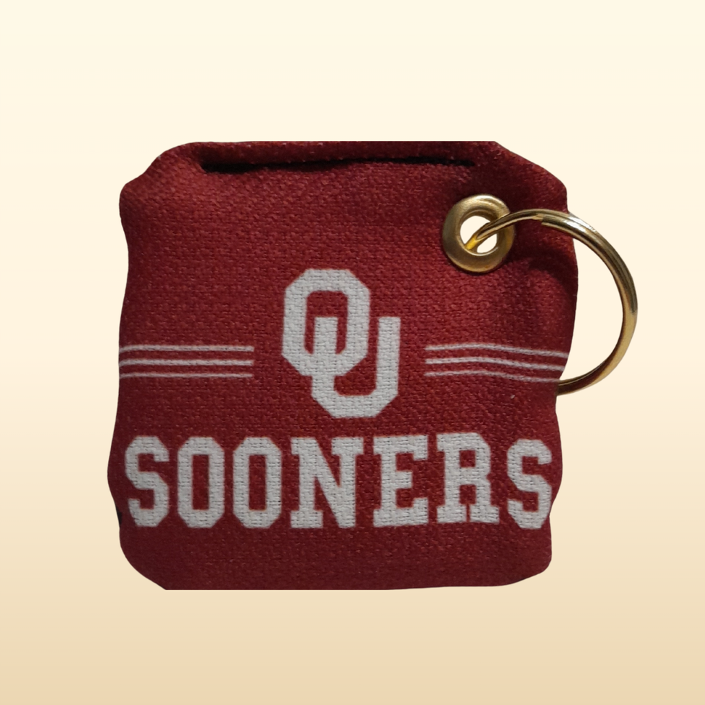 Red keychain with 'OU Sooners' text and gold ring on beige background