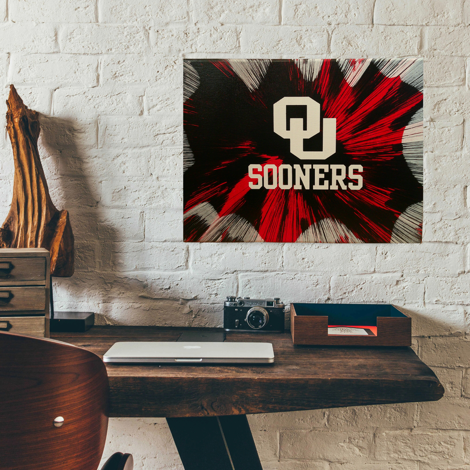 Desk with an Oklahoma Sooners Spin Art against a white brick wall
