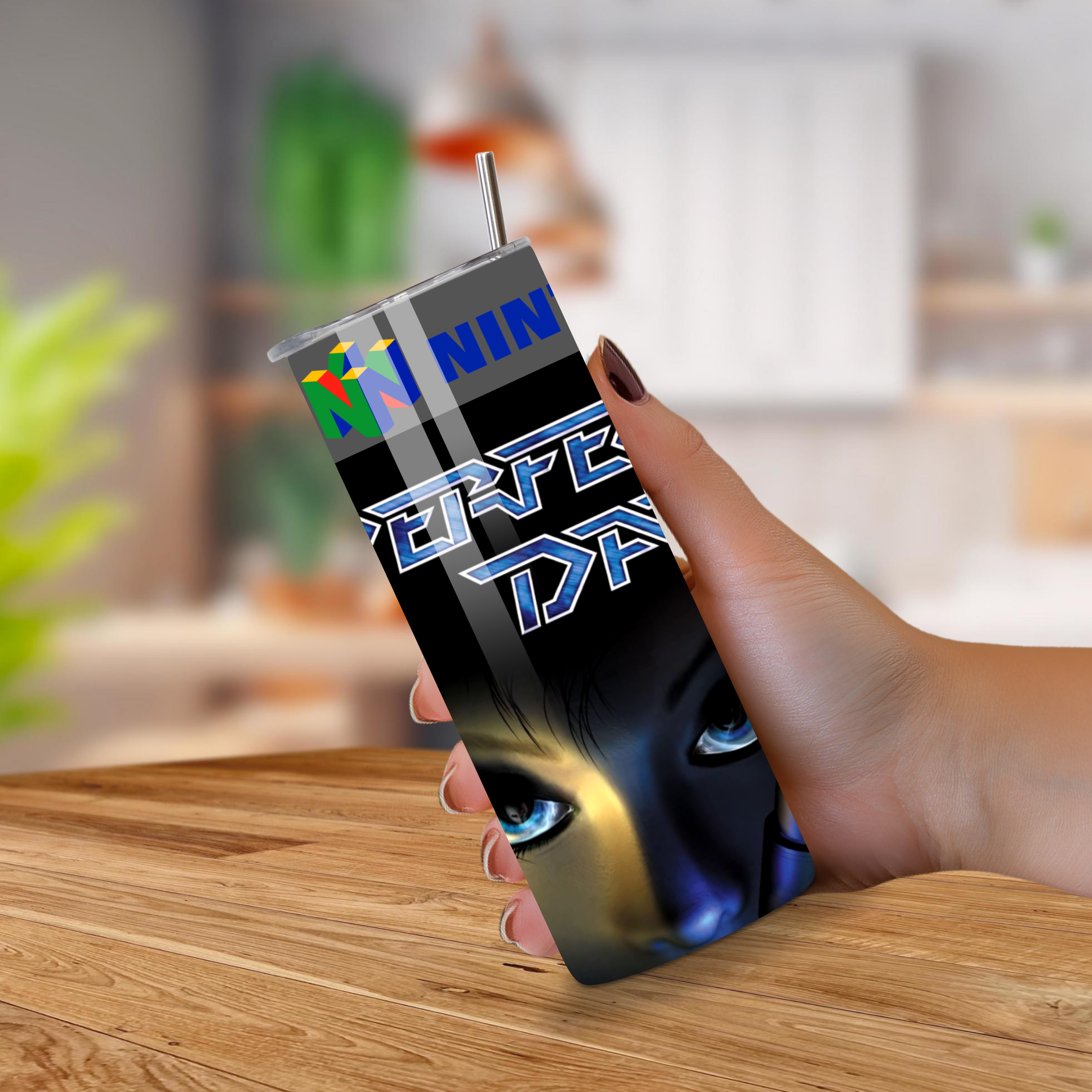 Person holding a tumbler with a Nintendo 64 Perfect Dark design and text, blurred indoor background