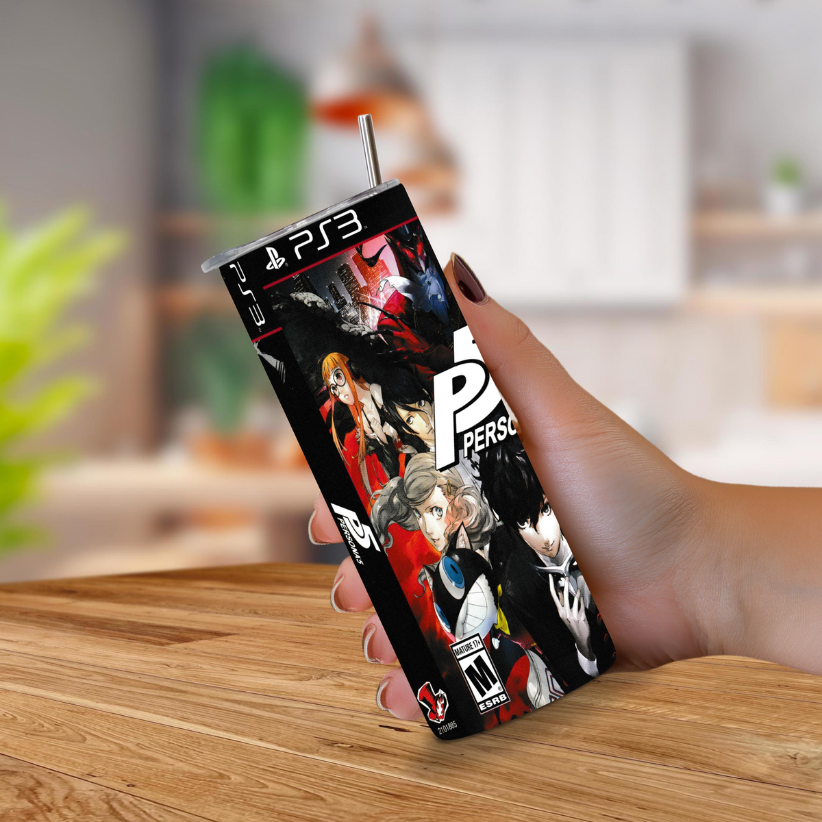 A hand holding a PS3-themed 20oz stainless steel with a straw, featuring character artwork from Persona 5, set against a blurred indoor background.
