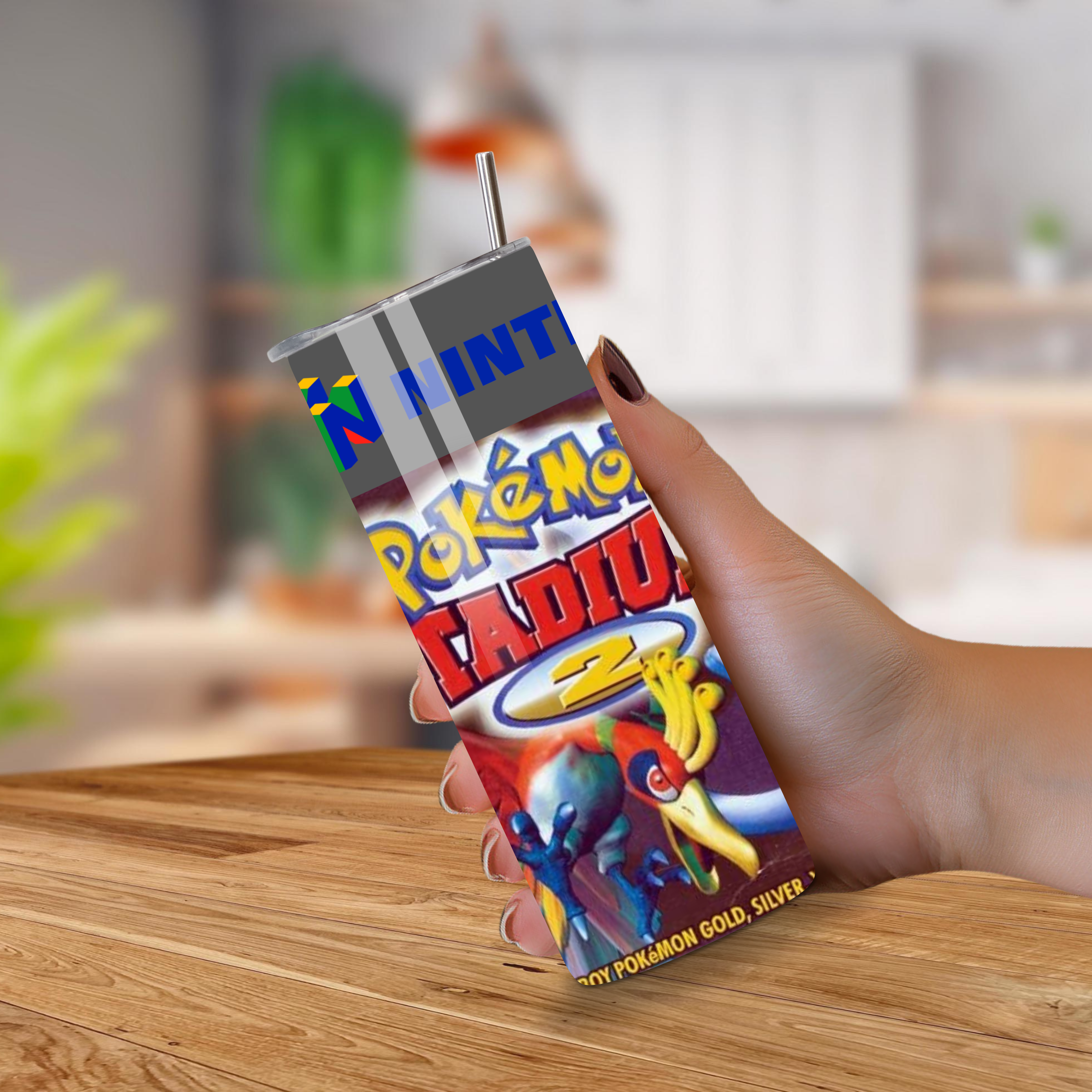 Hand holding a Pokémon Stadium 2 game tumbler on a wooden surface with a blurred background