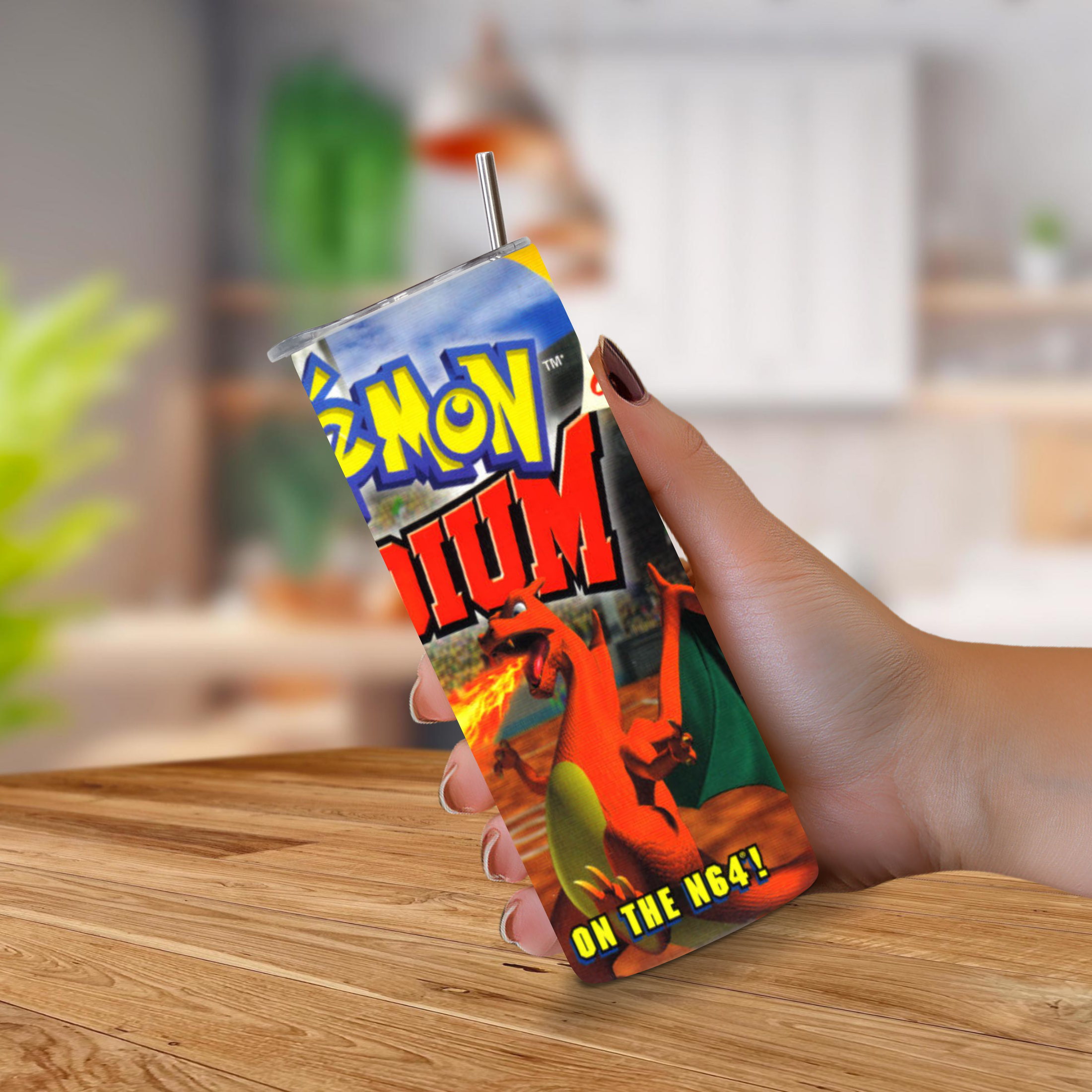 A hand holding a custom Pokemon Stadium 20oz stainless steel tumbler with a metal straw, set against a blurred kitchen background.