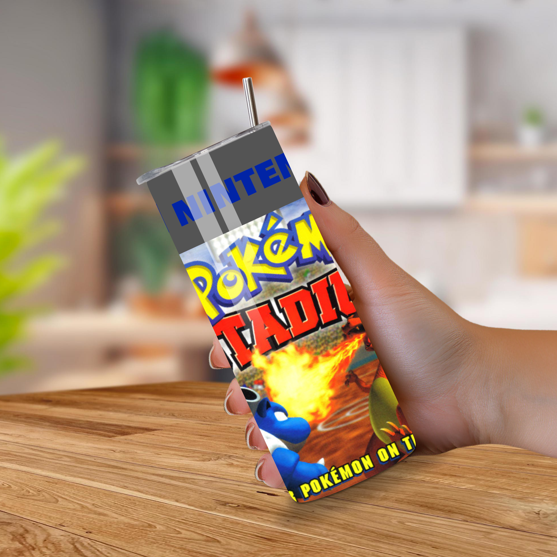 Person holding a tumbler with a 'Pokémon Stadium' design on a wooden surface.