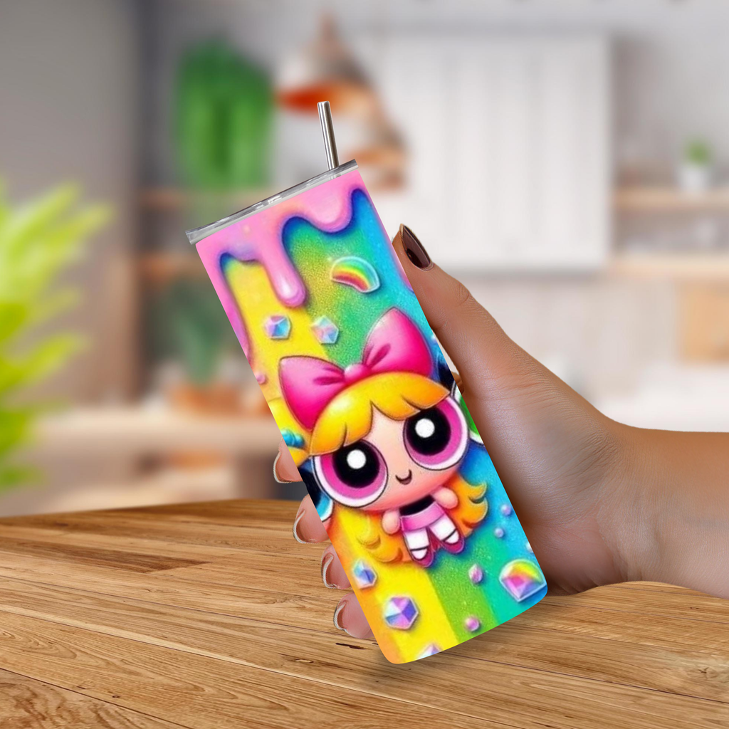 A hand holding a 20oz tumbler with a metal straw, decorated with a colorful cartoon character from Power Puff Girls and rainbow drip design, set against a blurred indoor background.