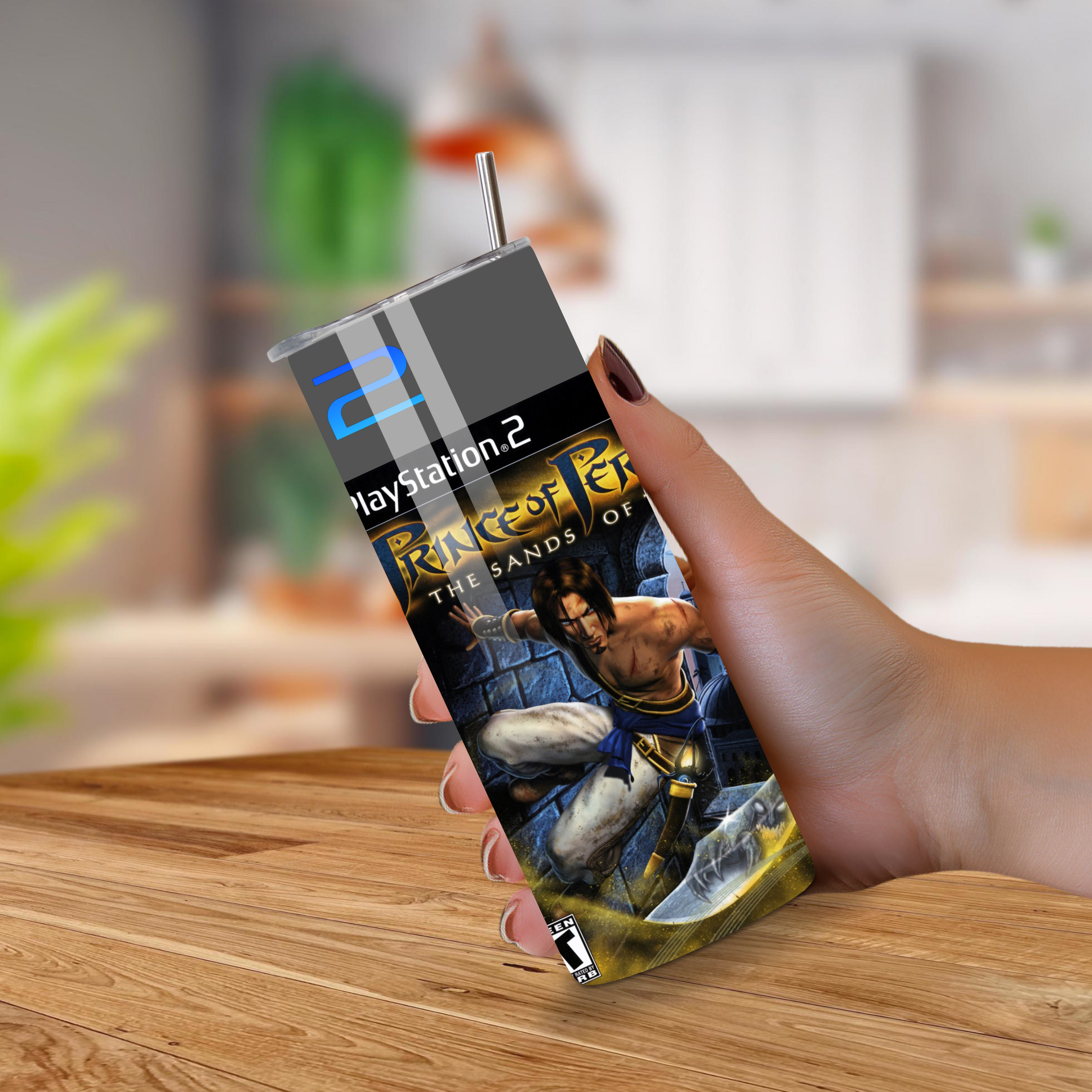 PlayStation 2 Tumbler with 'Prince of Persia' cover held by a hand on a wooden surface.