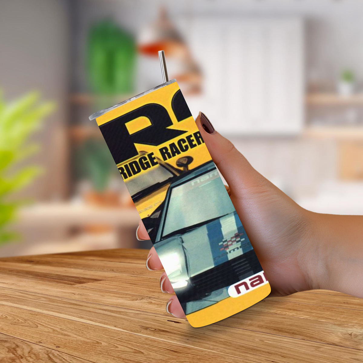 A hand holding a 20oz tumbler featuring a yellow and black PS1 'Ridge Racer Type 4' theme with a car graphic, set against a blurred indoor background.