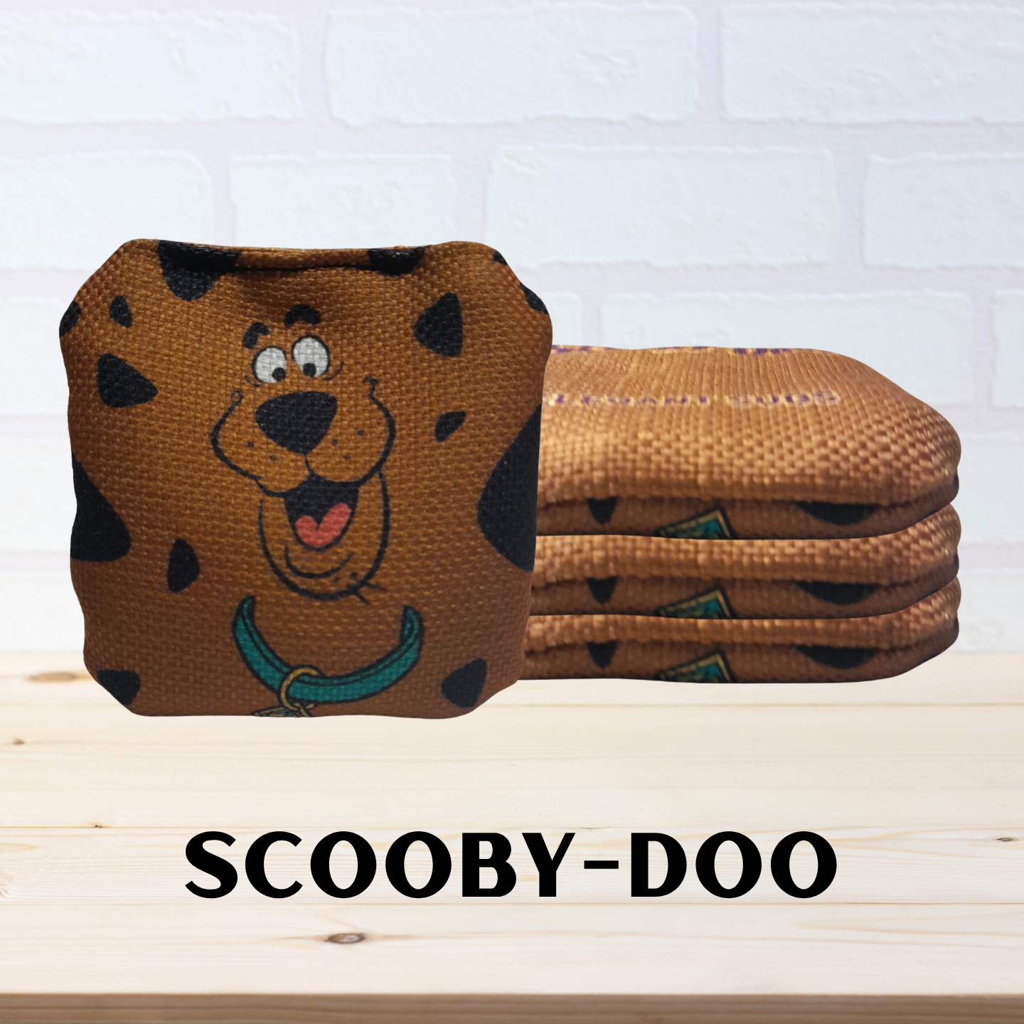 Mini cornhole bags with Scooby-Doo design on a white brick wall background