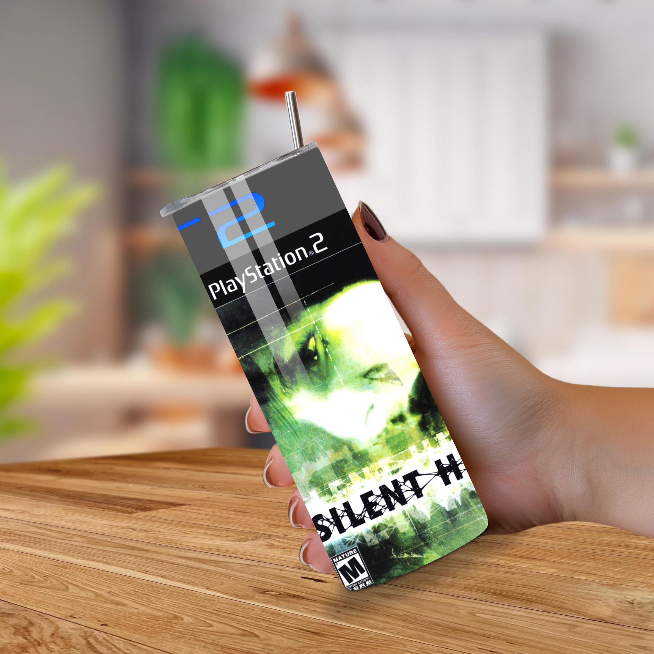 Hand holding a PlayStation 2 20oz tumbler with 'Silent Hill 2' design on a wooden surface.