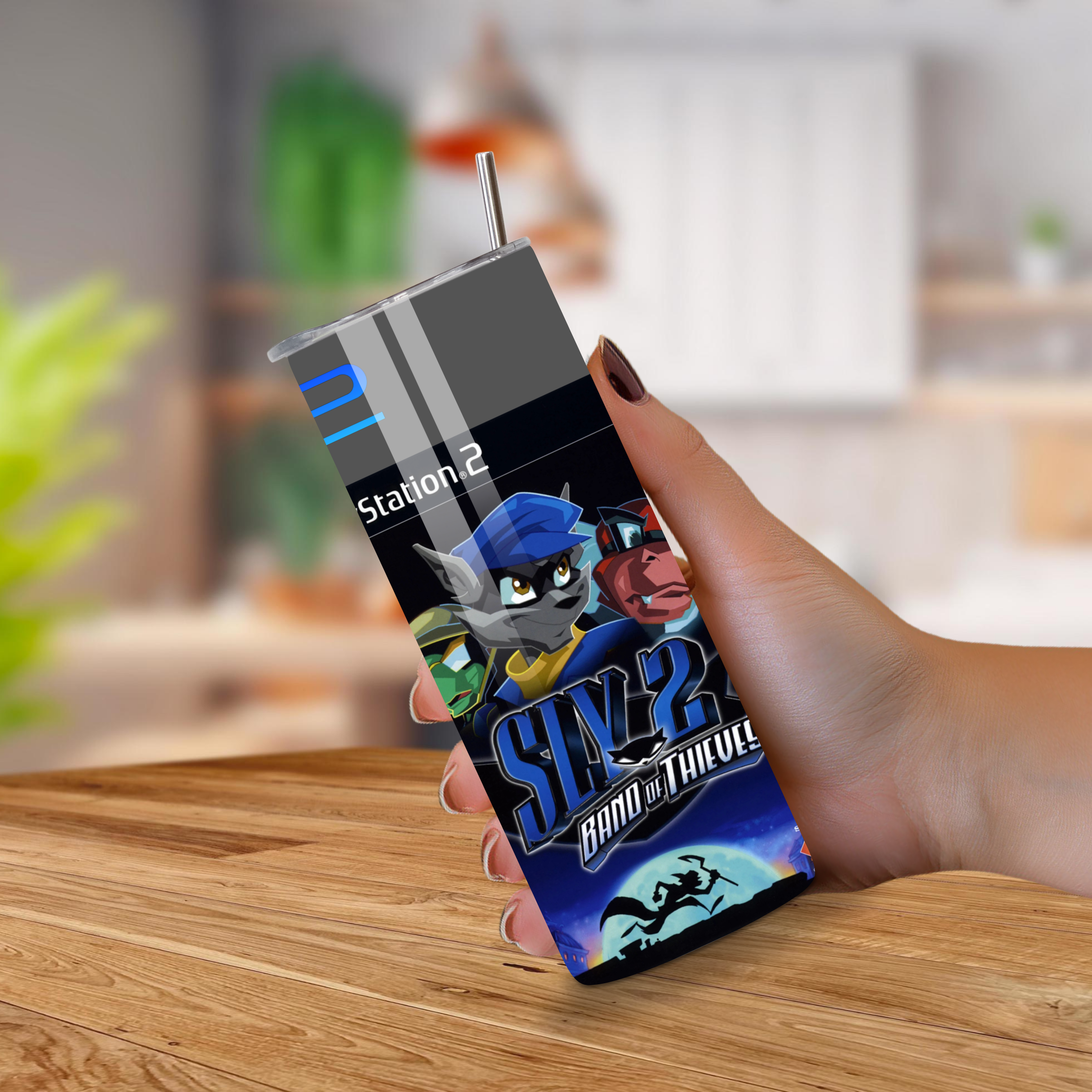 Hand holding a 20oz tumbler with 'Sly 2: Band of Thieves' design on a wooden surface.