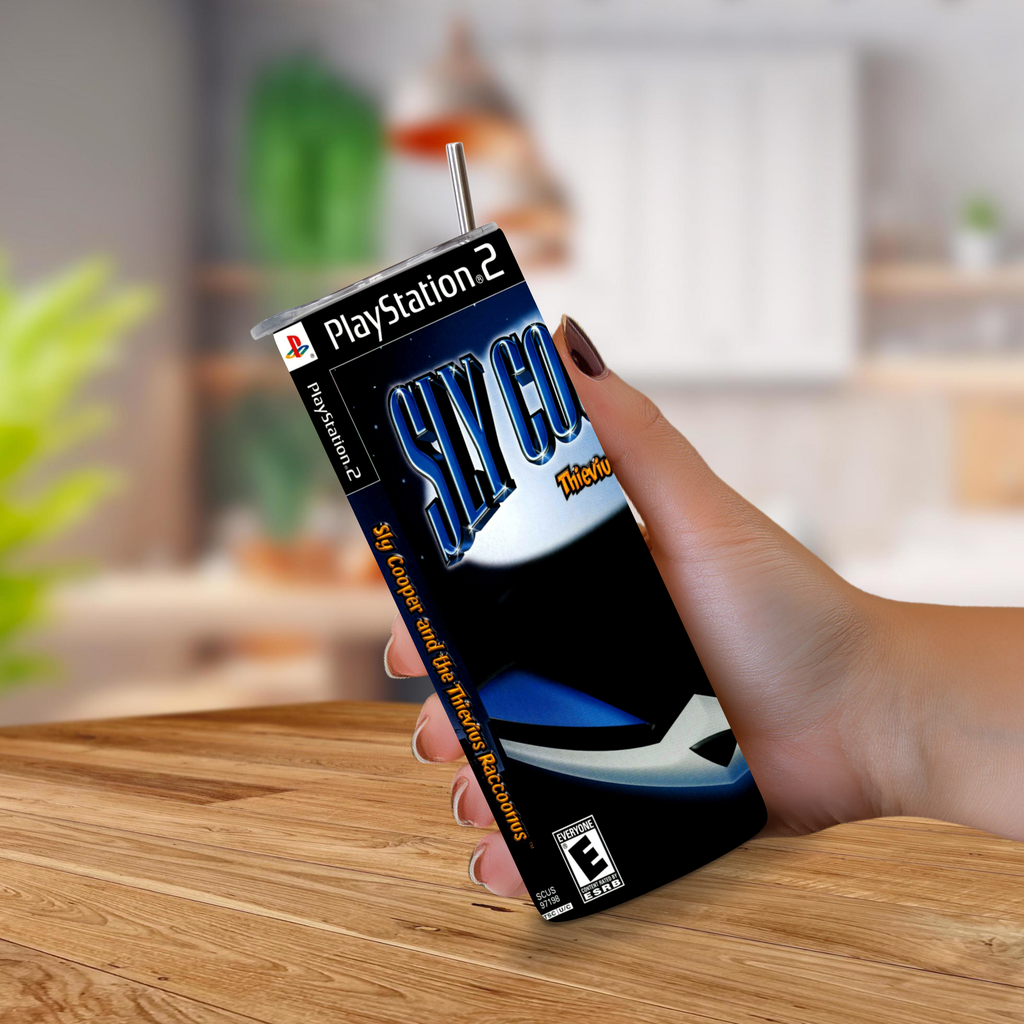 A hand holding a 20oz tumbler with PlayStation 2 Sky Cooper theme on a wooden table with a blurred indoor background.