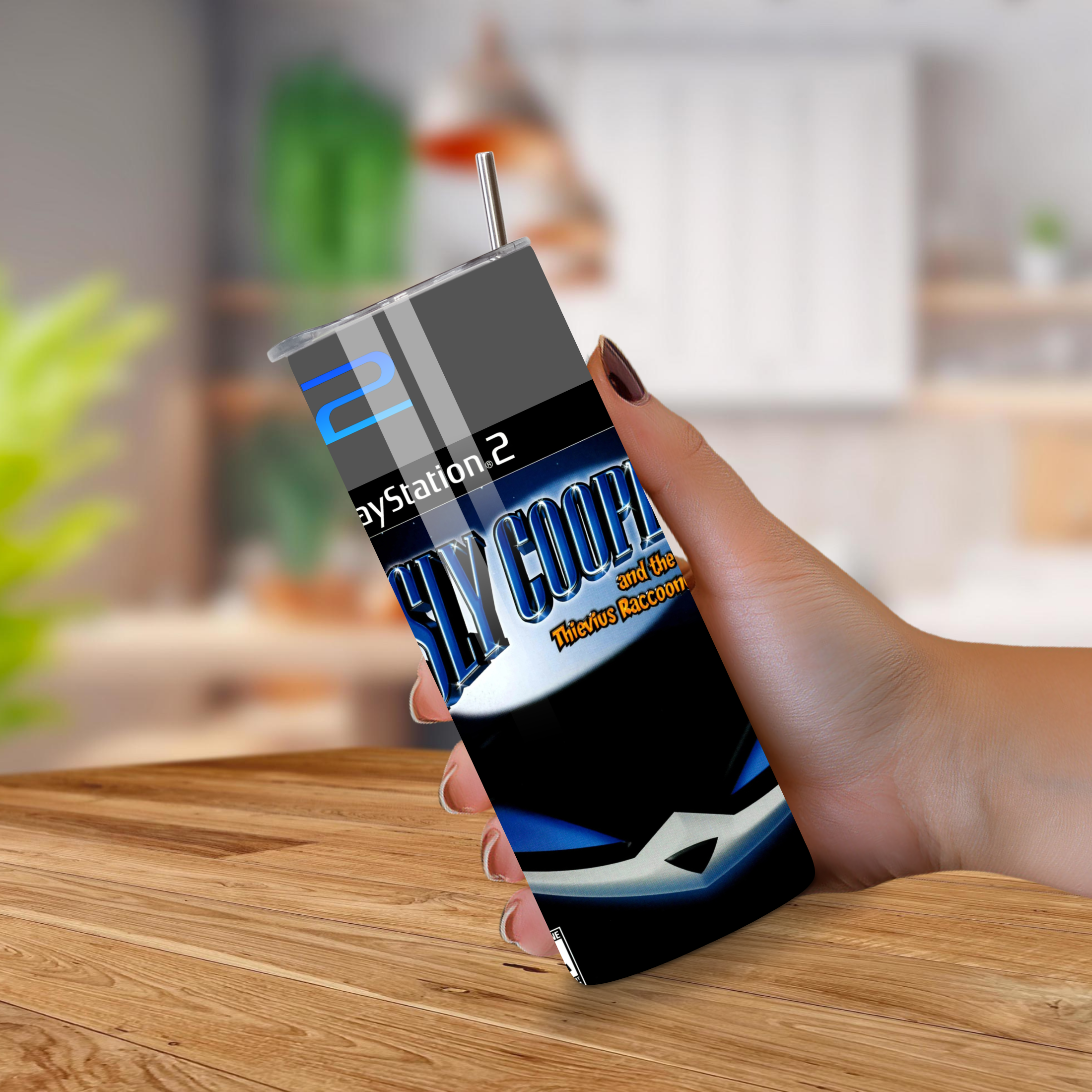 Person holding a tumbler with PlayStation 2 Sly Cooper design on a wooden surface.