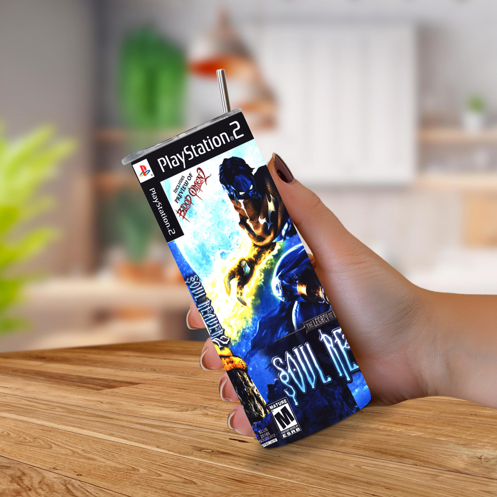 A hand holding a 20oz tumbler PlayStation 2 designed to look Soul Reaver 2 with a metal straw sticking out of the top, set against a blurred kitchen background.