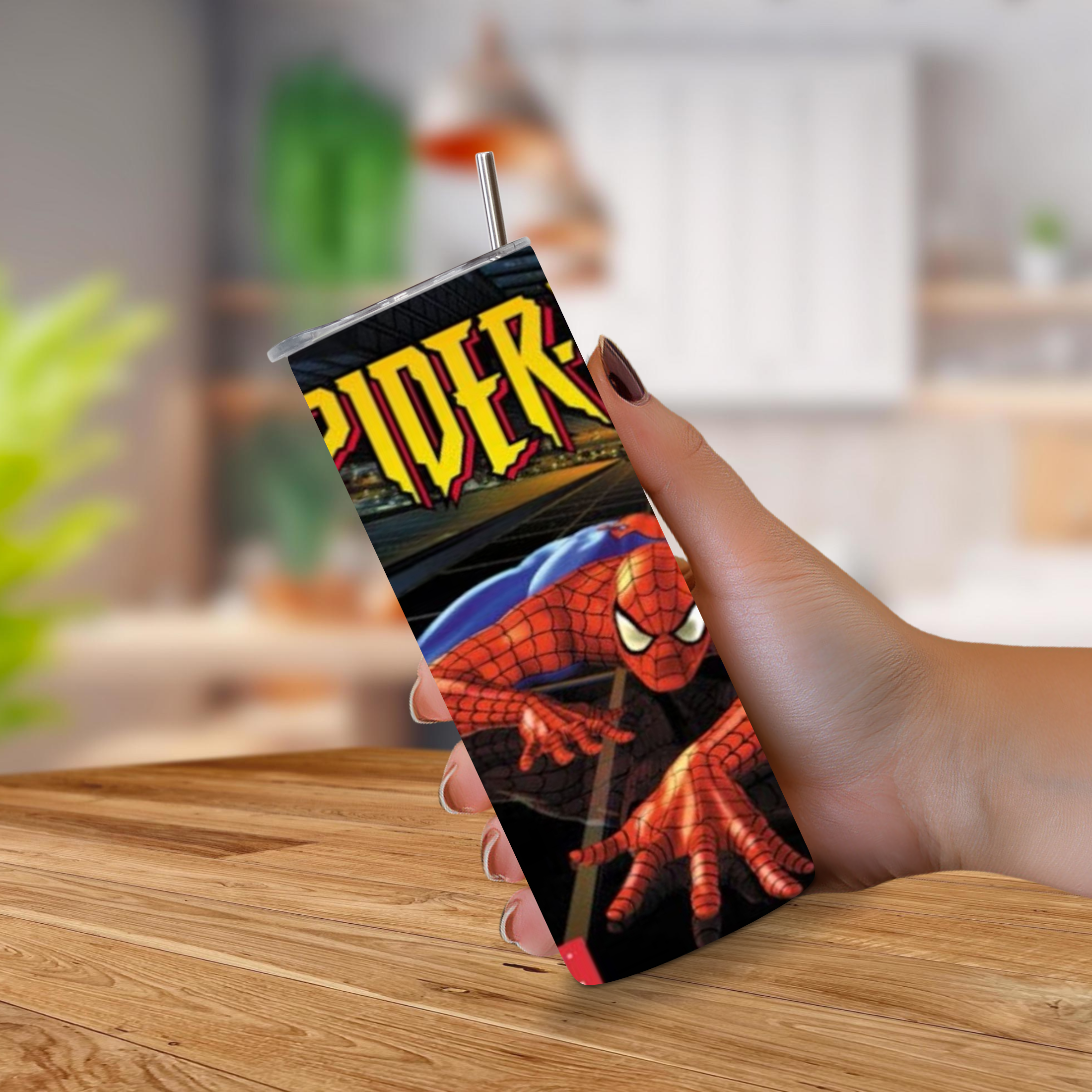 A hand holding a 20oz tumbler featuring a Spider-Man graphic print, with a metal straw, set against a blurred kitchen background.