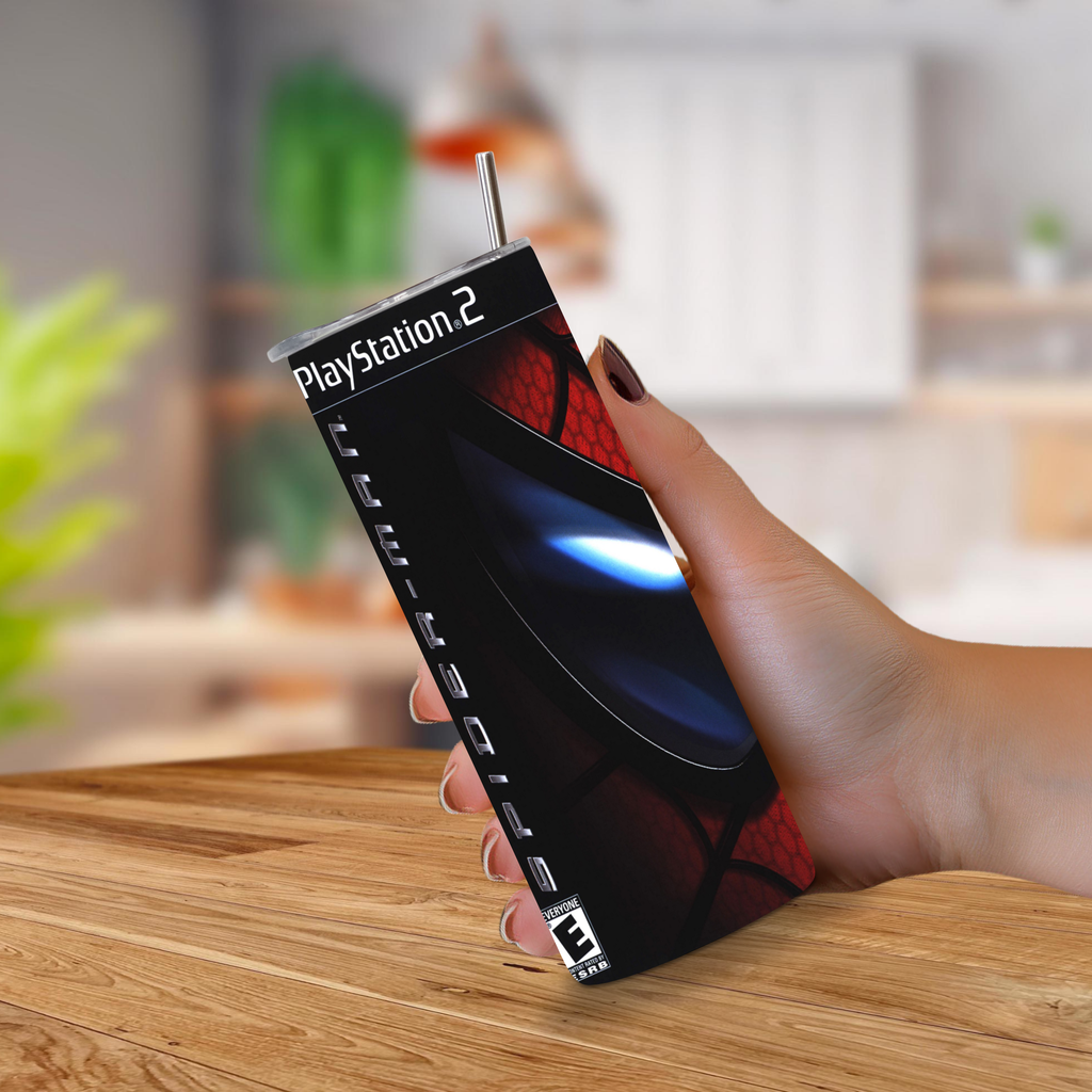 A hand holding a PlayStation 2 20oz tumbler in a kitchen setting, with the console wrapped in a custom red and black Spider-Man themed skin.
